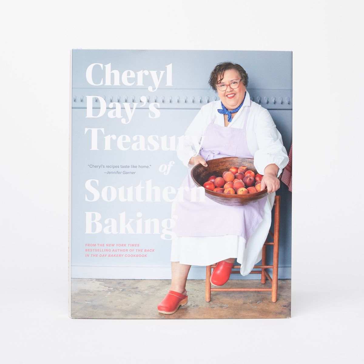Cover of a cookbook that reads "Cheryl Day's Treasury of Southern Baking" over a photo of a person sitting in a chair holding a large wooden bowl of peach