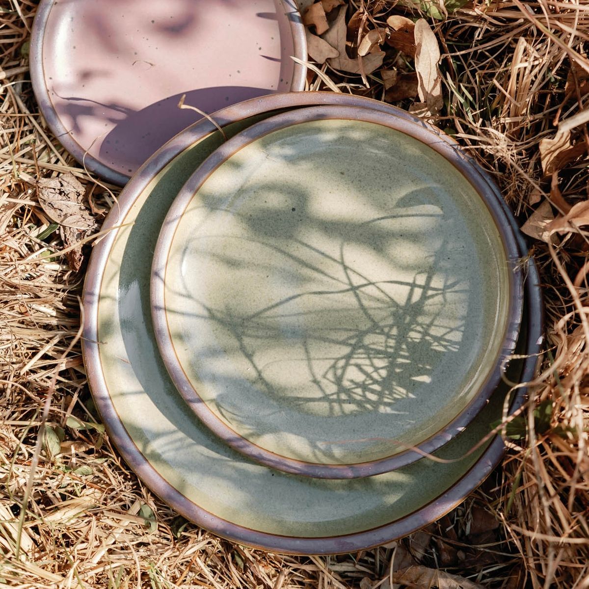 Dusty mauve pink ceramic platter arranged in dry grass and wild plants outdoors.