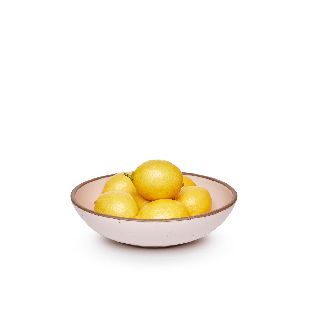 A dinner-sized shallow ceramic bowl in a soft light pink color featuring iron speckles and an unglazed rim, filled with lemons