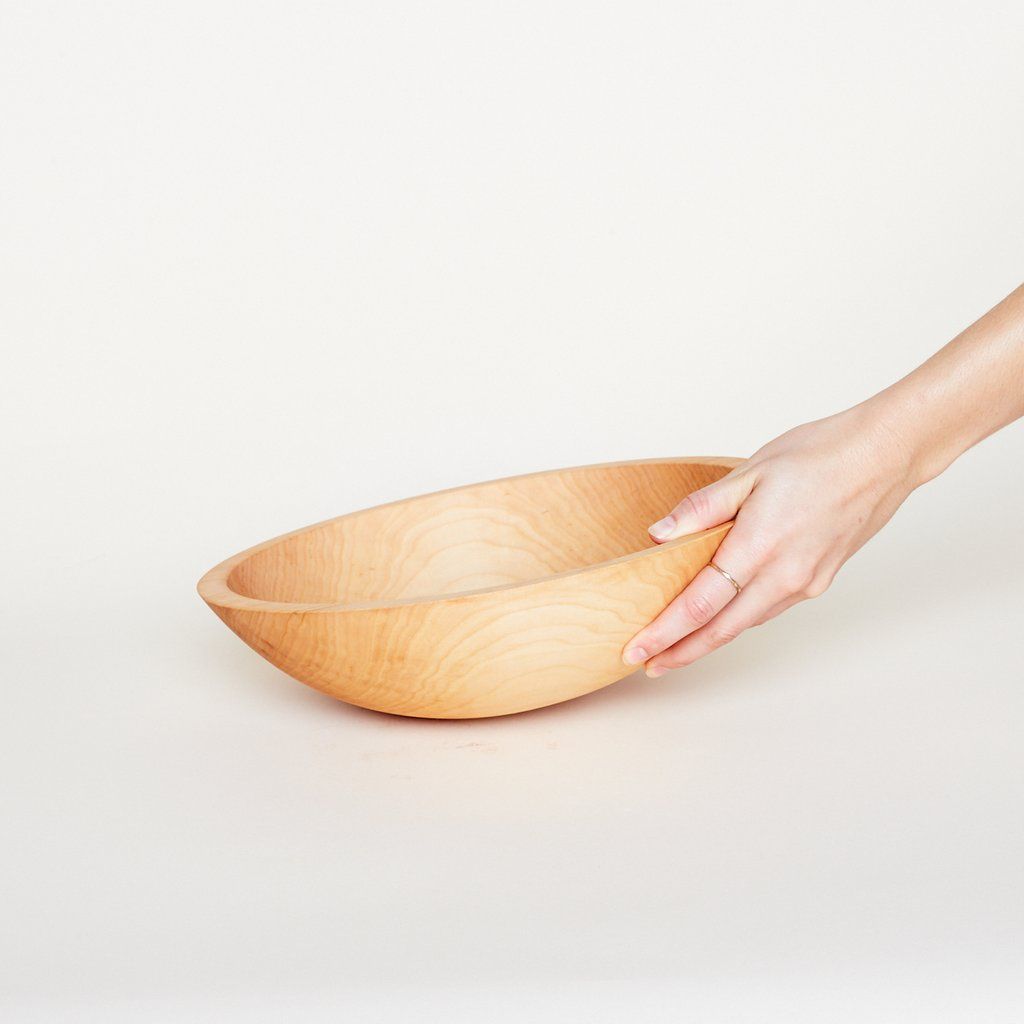 A hand touches a medium-sized light-colored wooden bowl