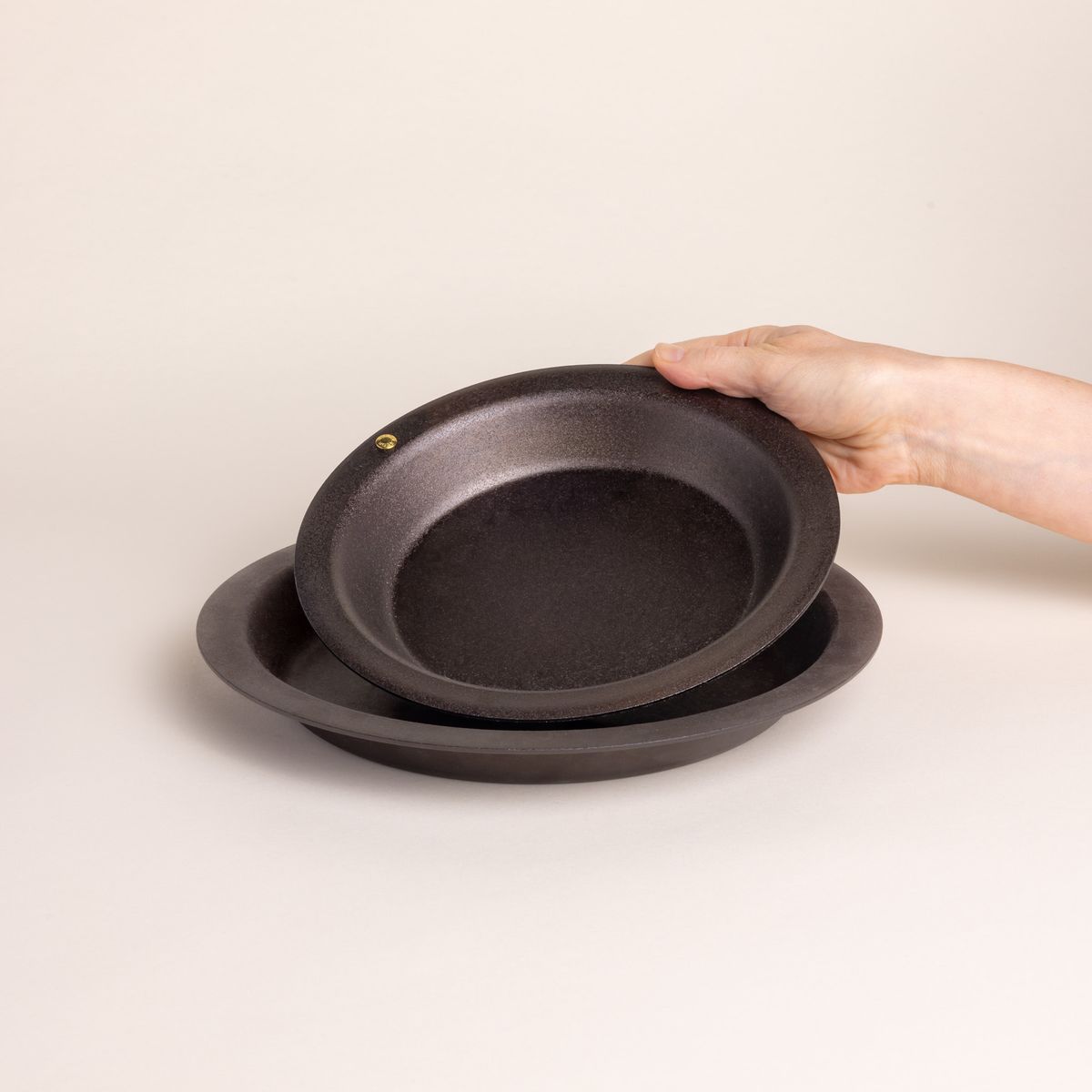 A hand places a simple cast iron pie dish to nest into a larger one.