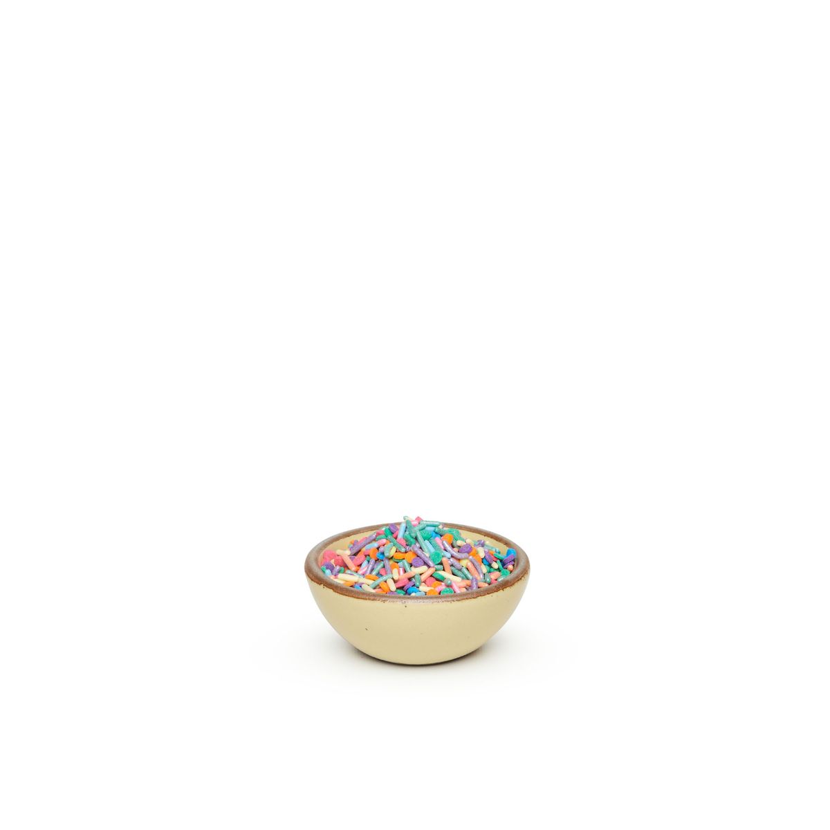A tiny rounded ceramic bowl in a light butter yellow color featuring iron speckles and an unglazed rim, filled with sprinkles