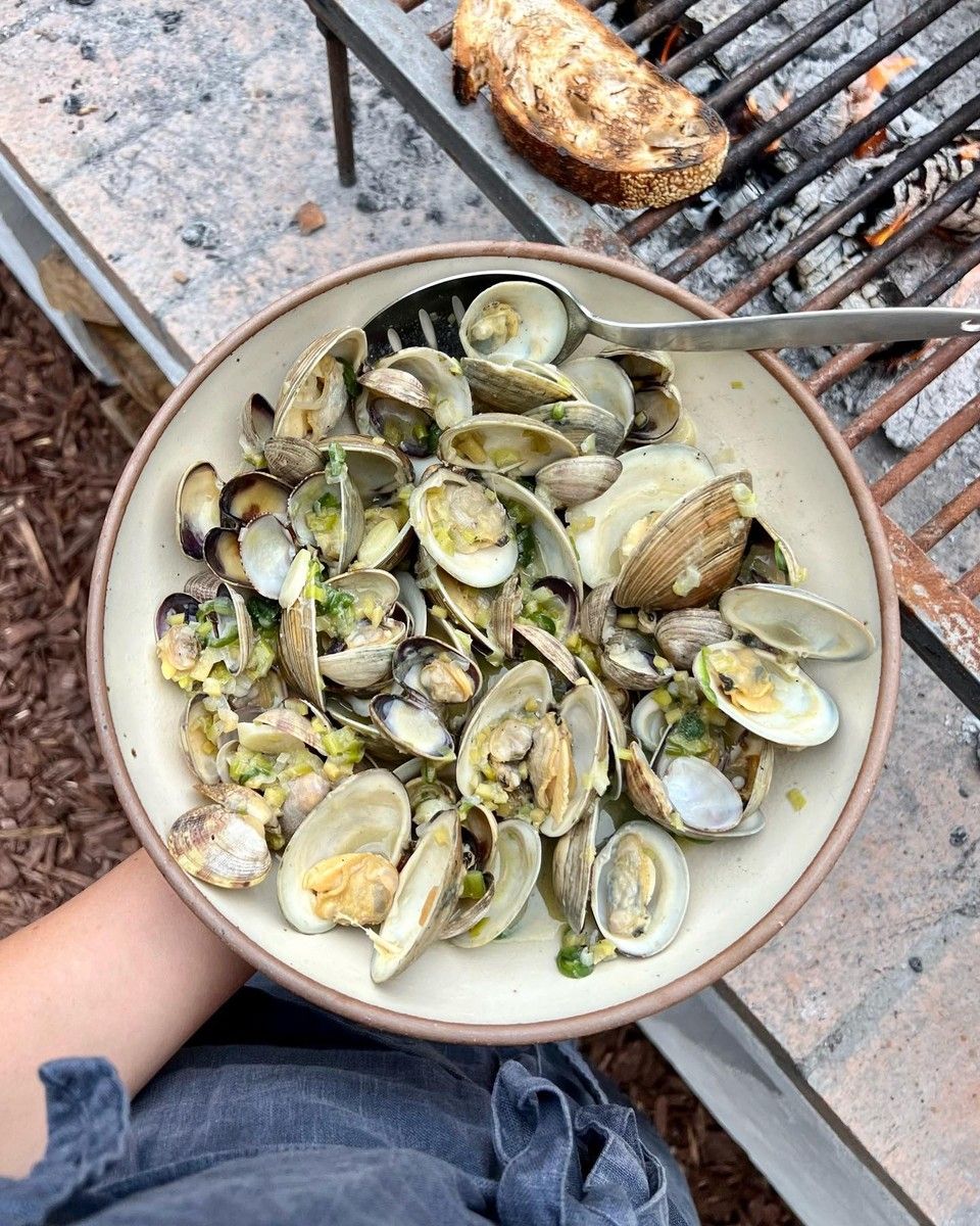 Outside, a hand holds a ceramic coupe plate filled with mussels