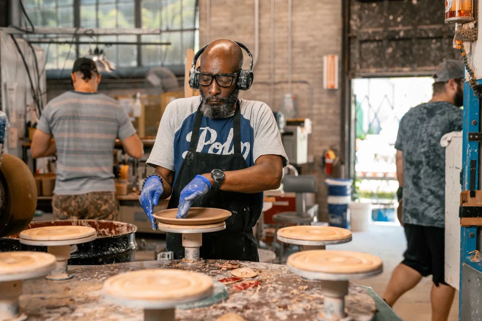 A factory room filled with machinery with a person in the foreground using his hands to smooth a clay plate