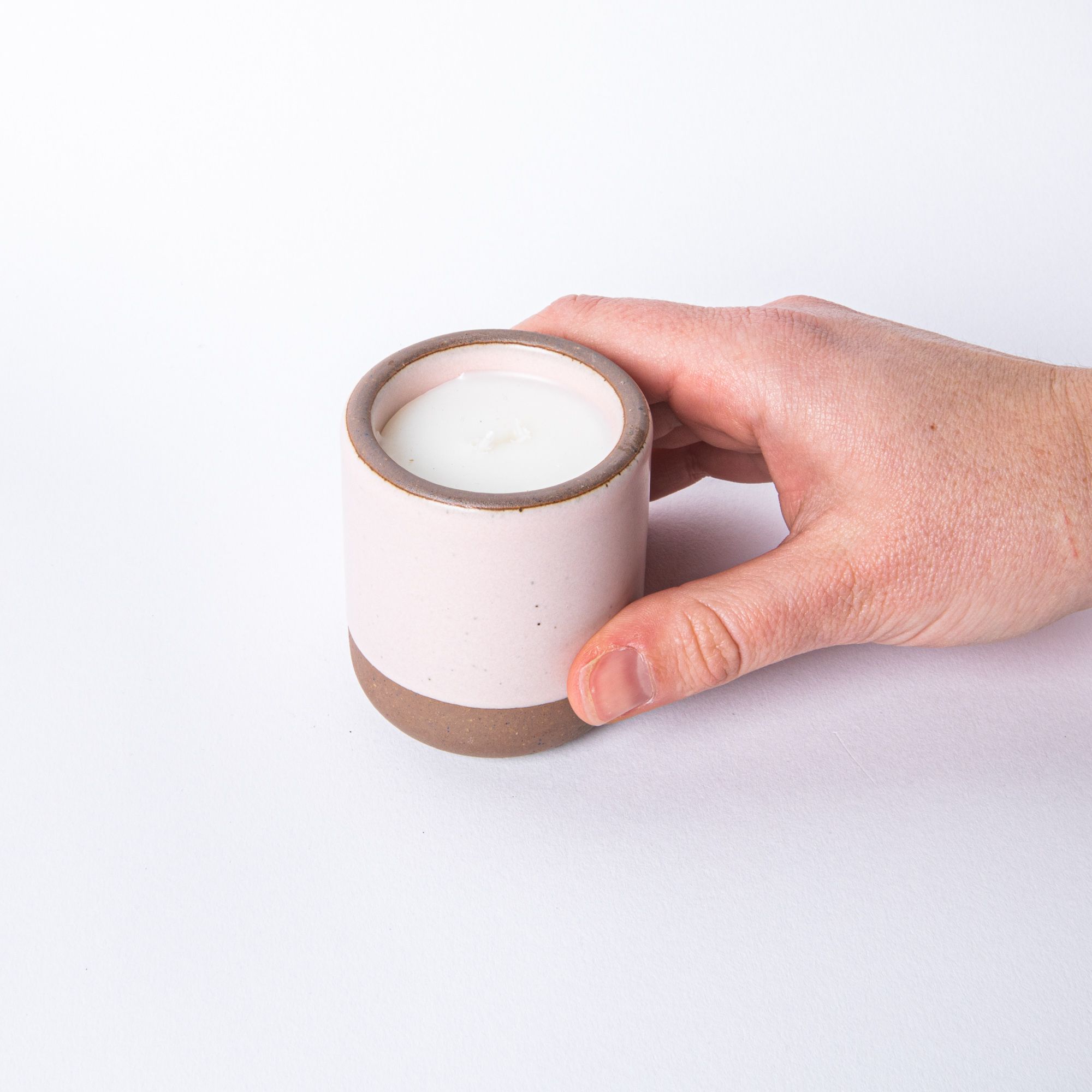 Hand holding a small ceramic vessel in soft light pink color with candle inside