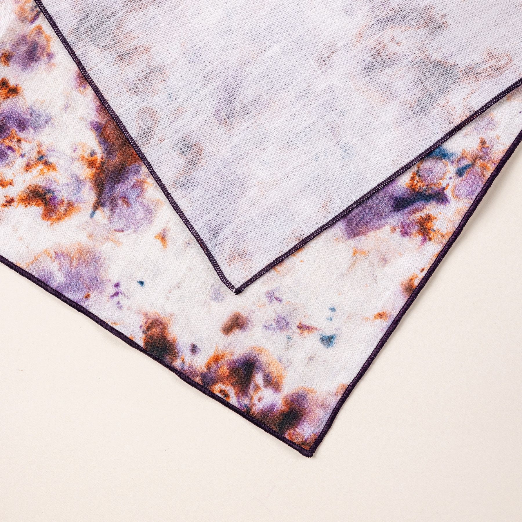 Close up of the front and back of a linen napkin in a marbled pattern with white, pink, purple, and orange colors