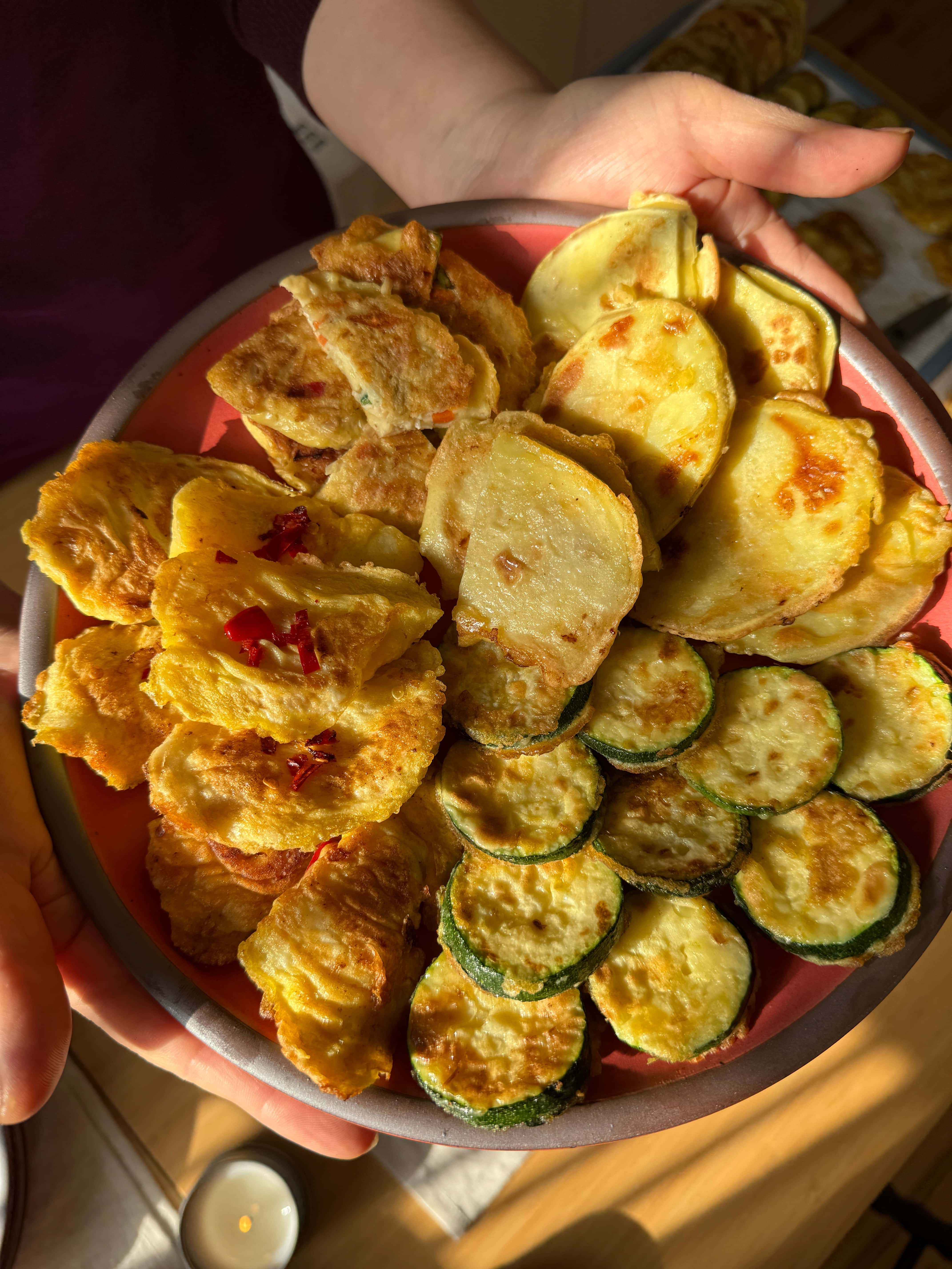 Hands hold out a plate of Korean Lunar New Year foods all stacked beautifully together, including Goguma Jeon.