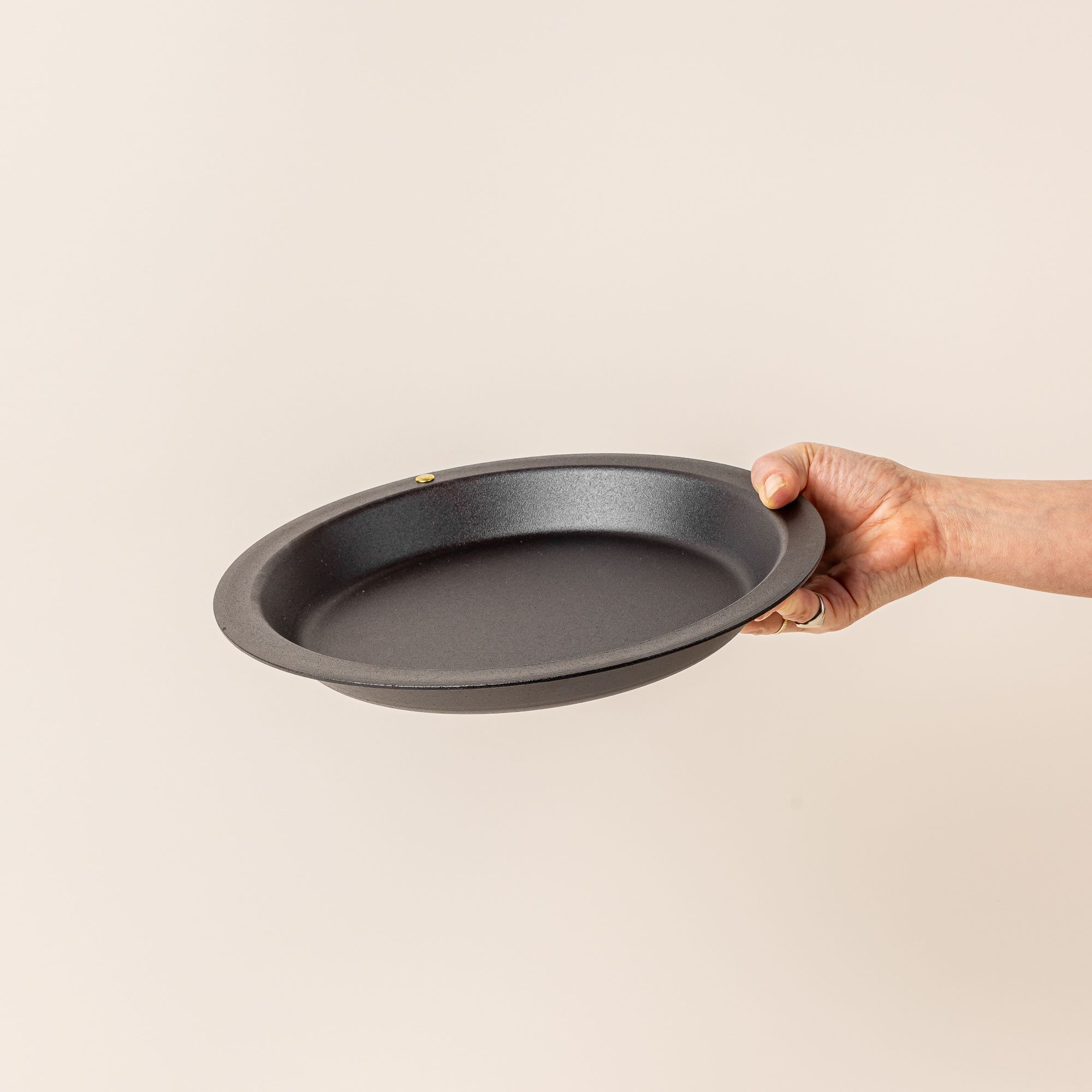 A hand holds a simple iron pie plate with a wide rim and shallow body