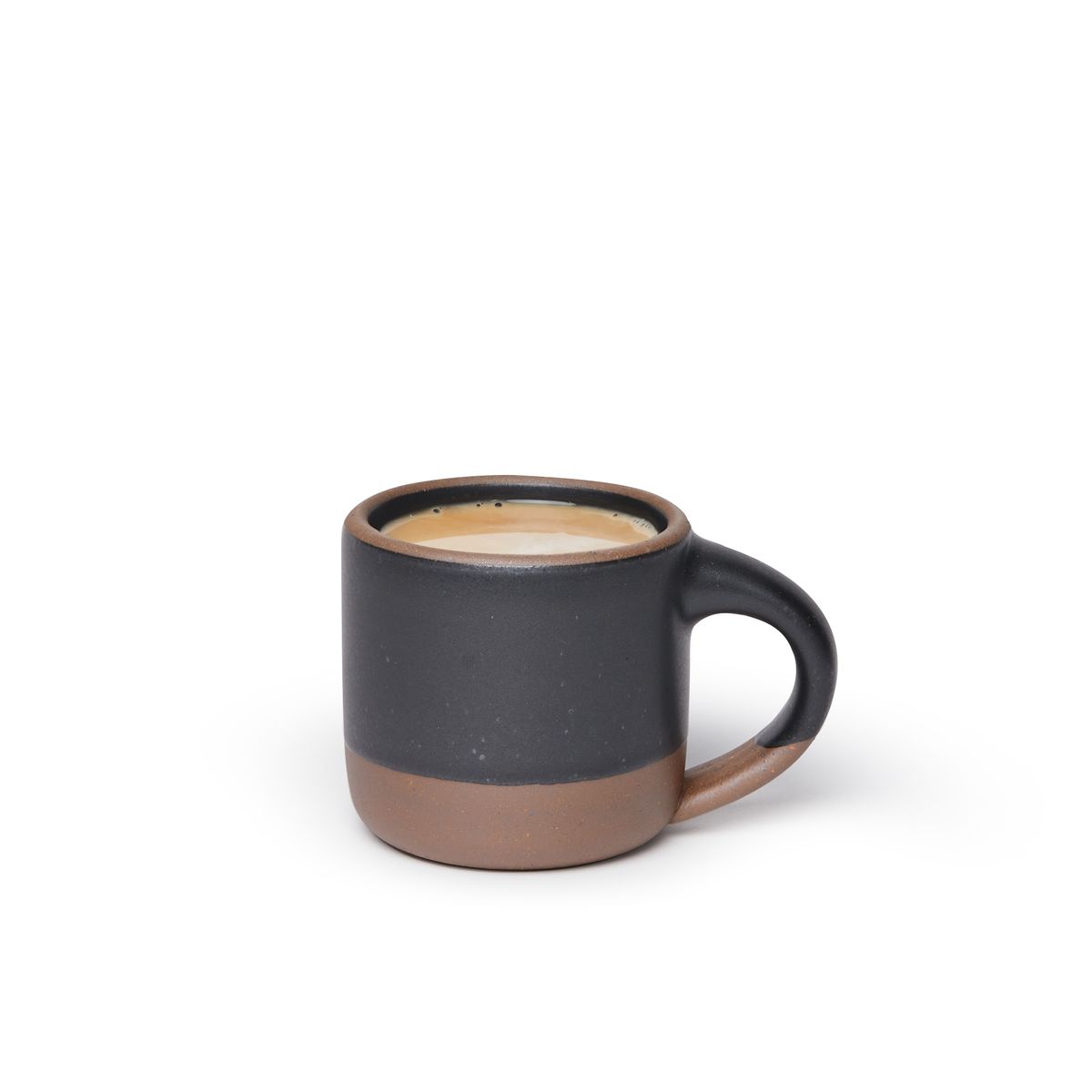 A small sized ceramic mug filled with coffee with handle in a graphite black glaze featuring iron speckles and unglazed rim and bottom base.