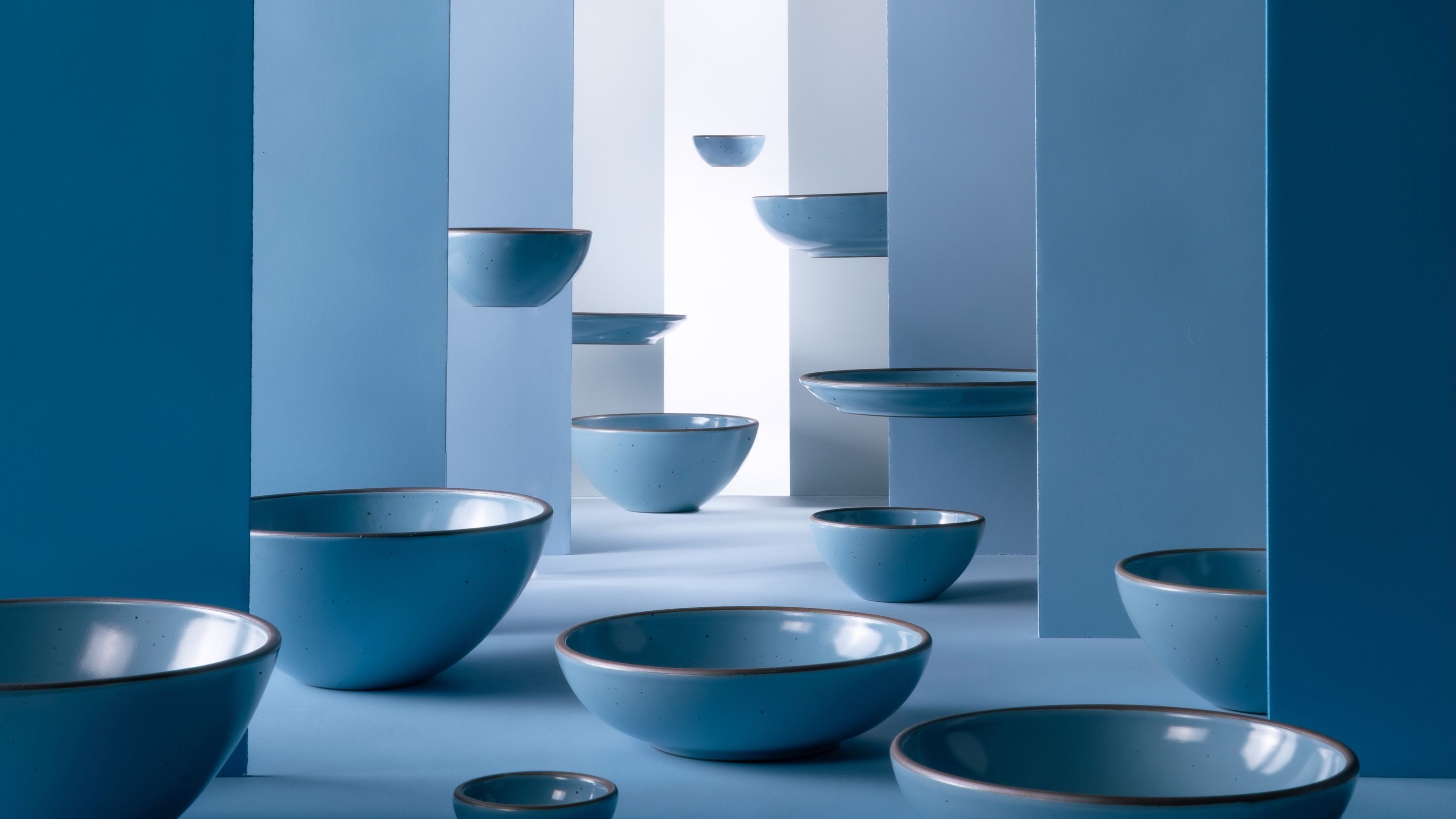 Ceramic bowls in a robin's egg blue color are artfully styled together among large walls in varying shades of blue. In the background, the bowls levitate in the air.