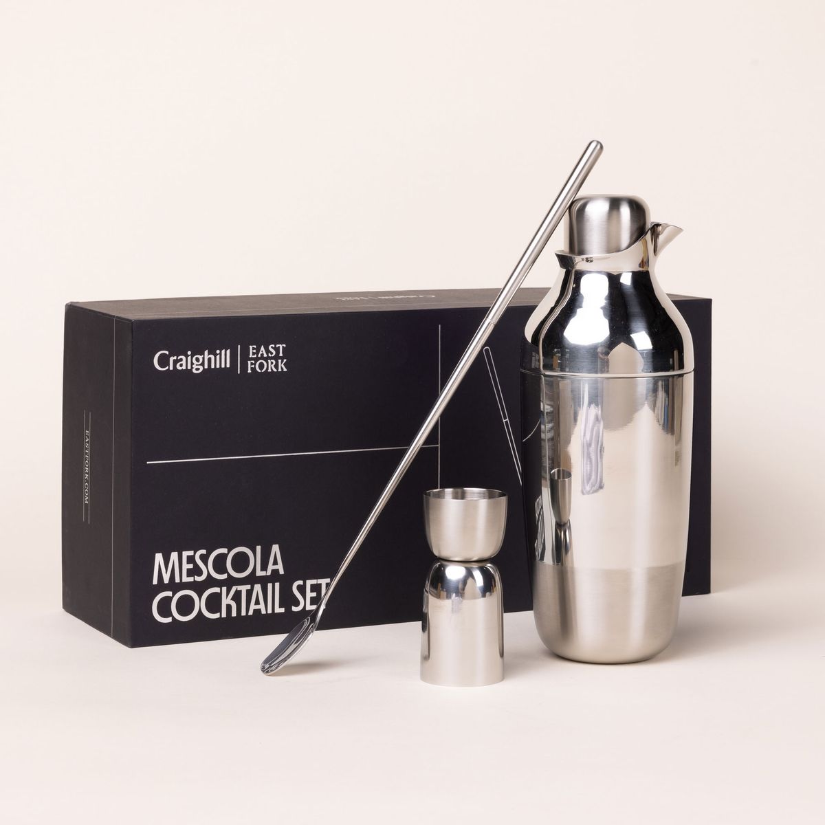 The Mescola Cocktail Set (including a stainless steel shaker, jigger, and cocktail spoon) sits in front of the black box packaging