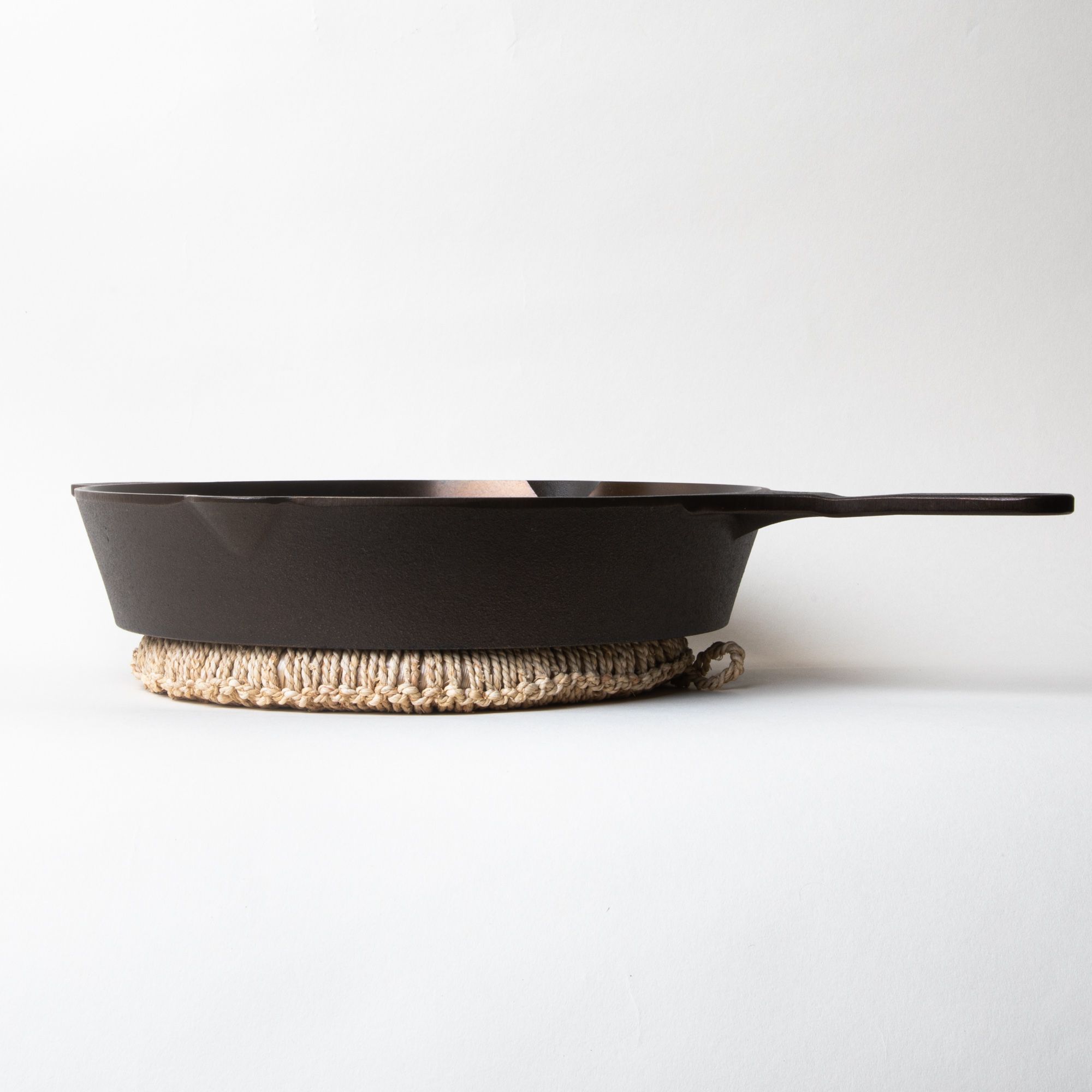 A cast iron skillet sitting on a circle ring trivet wrapped in woven organic material in a neutral color
