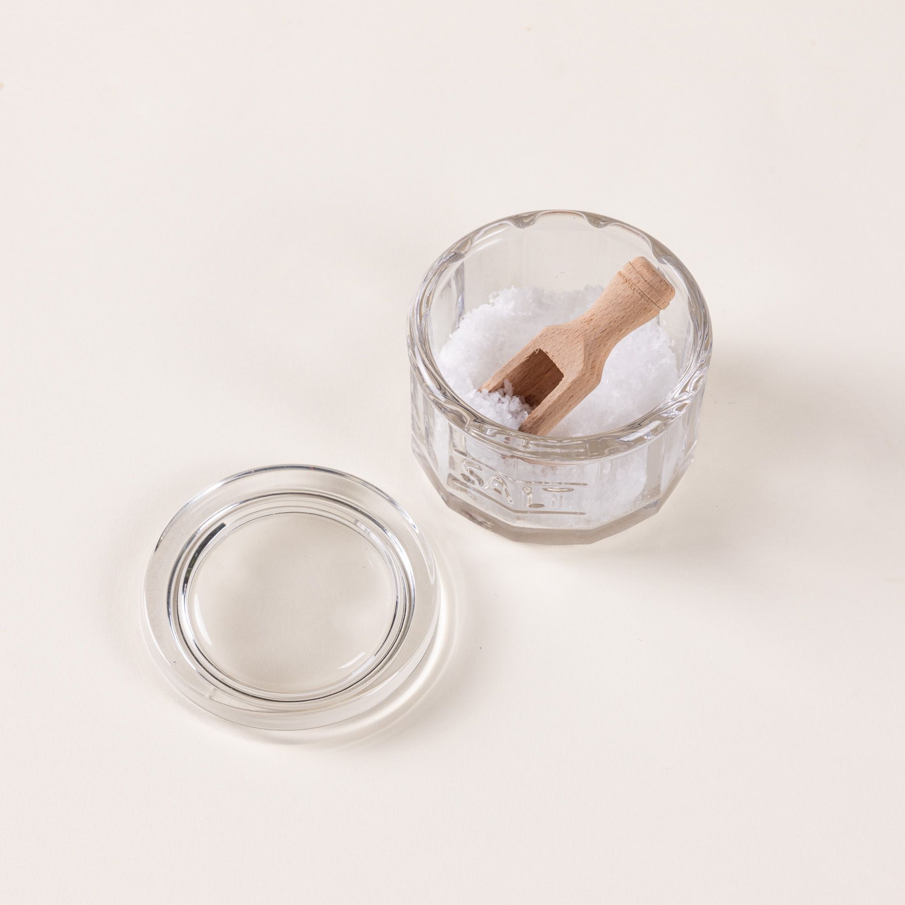 Round glass clear salt canister filled with salt and a small wooden scoop