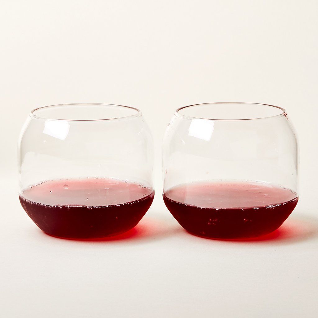 Two stemless wine glasses with a rounded shape, containing a bit of red, bubbly liquid