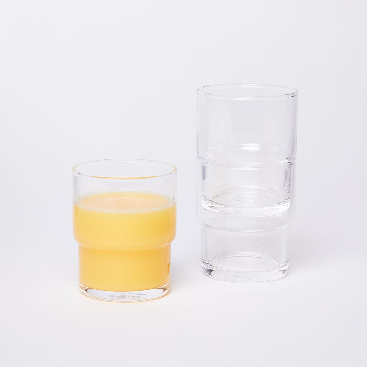 One glass on the left, full of orange juice, next to two stacked glasses on the right