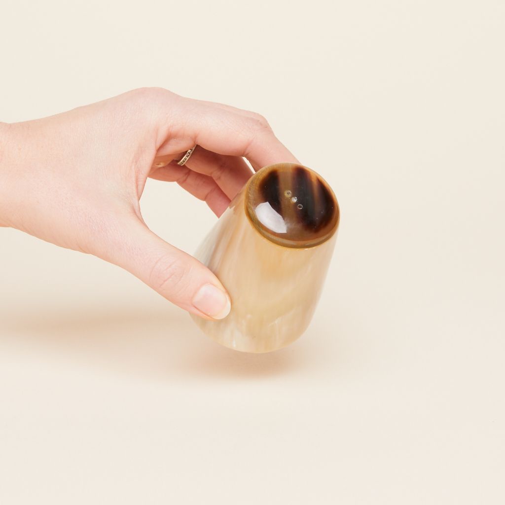A salt shaker with a dark brown circular top and a light brown cylindrical body is held at any angle by a hand