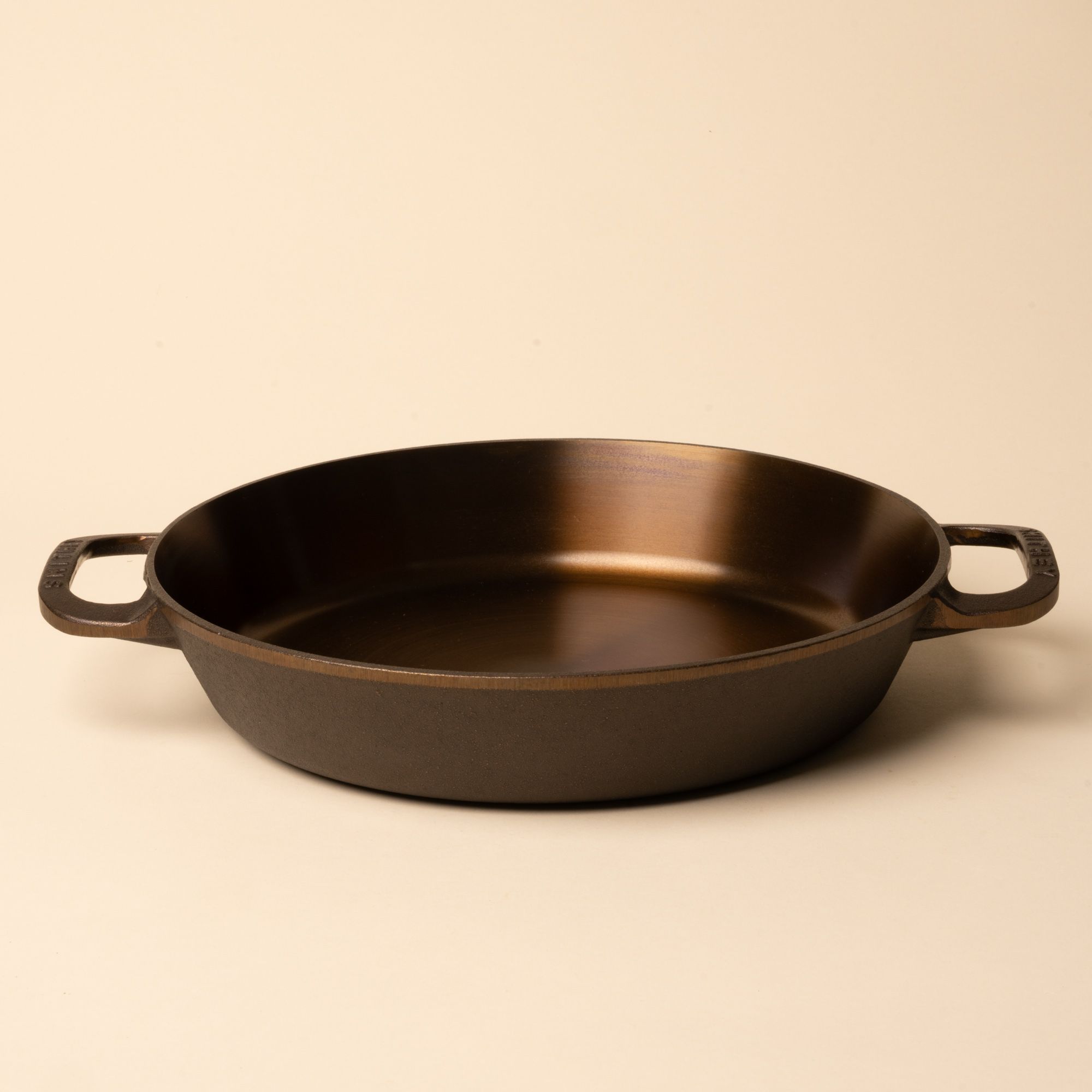 Round cast iron pan with two side handles on a beige background.