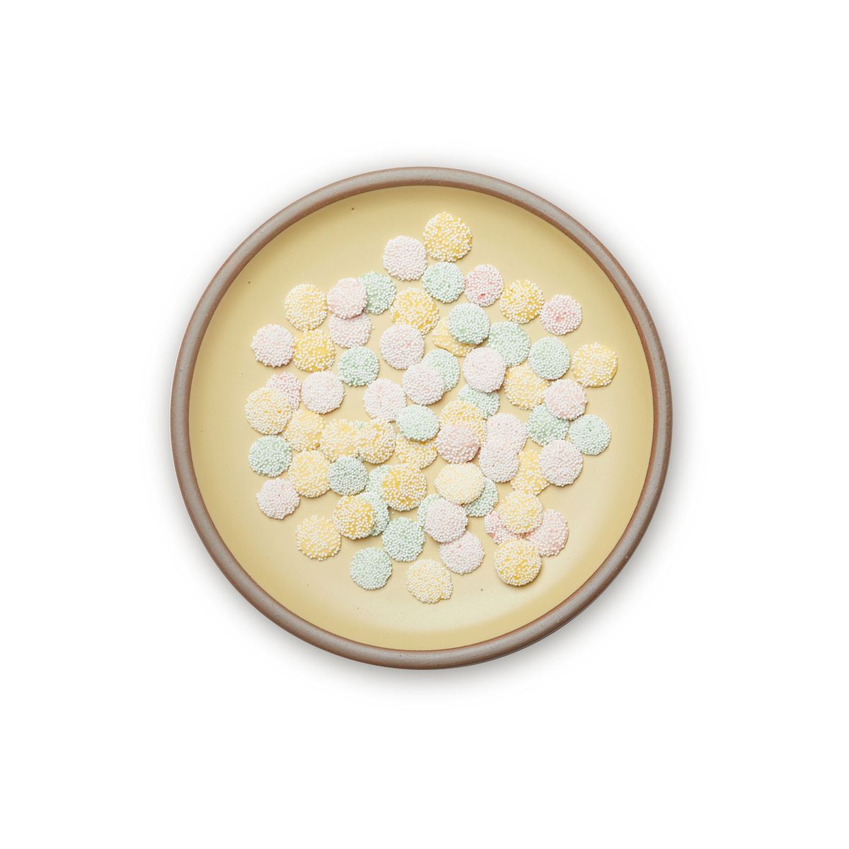 Little pastel candies on a dinner sized ceramic plate in a light butter yellow color featuring iron speckles and an unglazed rim
