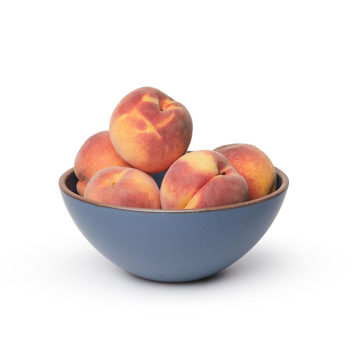 A large rounded ceramic bowl in a toned-down navy color featuring iron speckles and an unglazed rim, filled with peaches