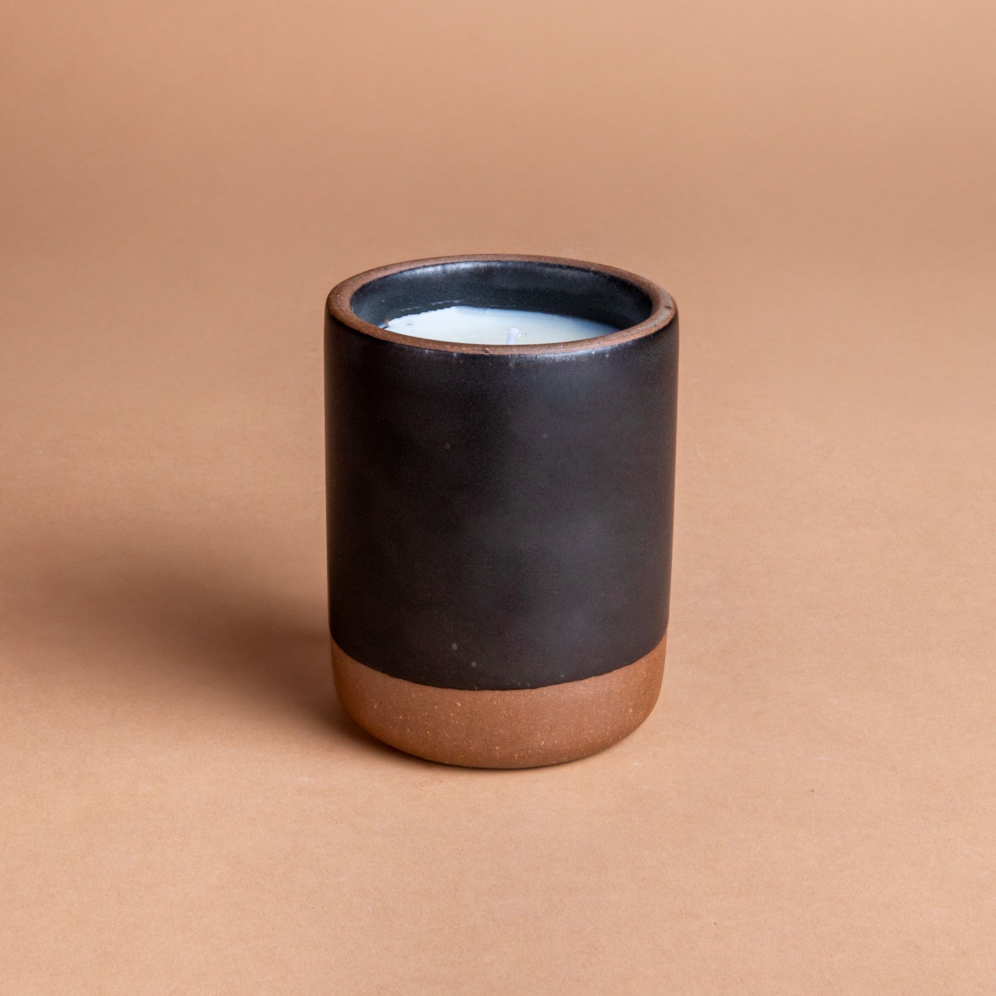 Large ceramic vessel in dark charcoal color with candle inside.