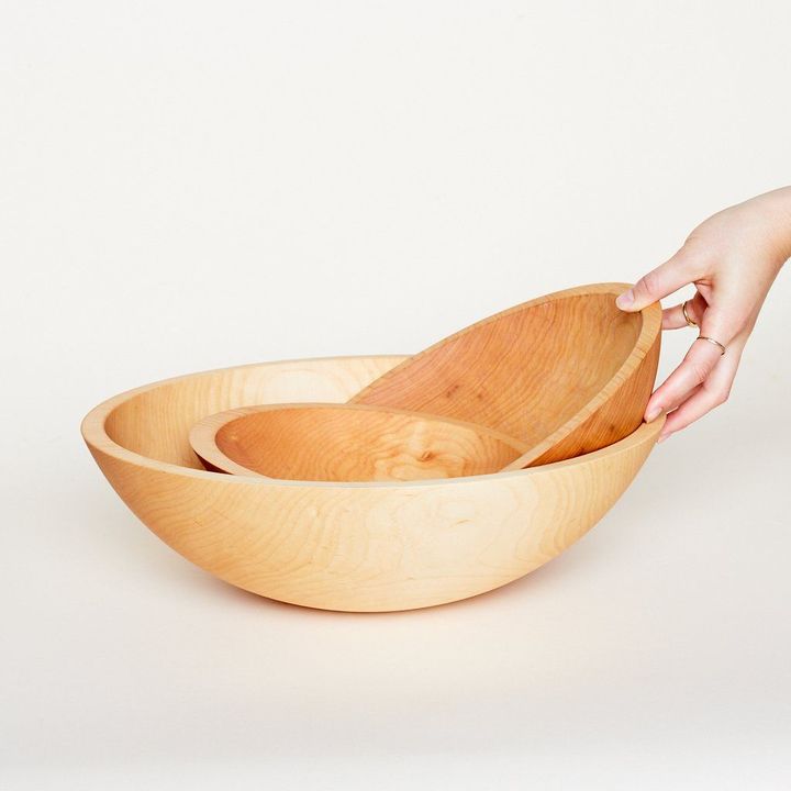 Three sizes of light wood bowls with a hand holding the medium-sized one