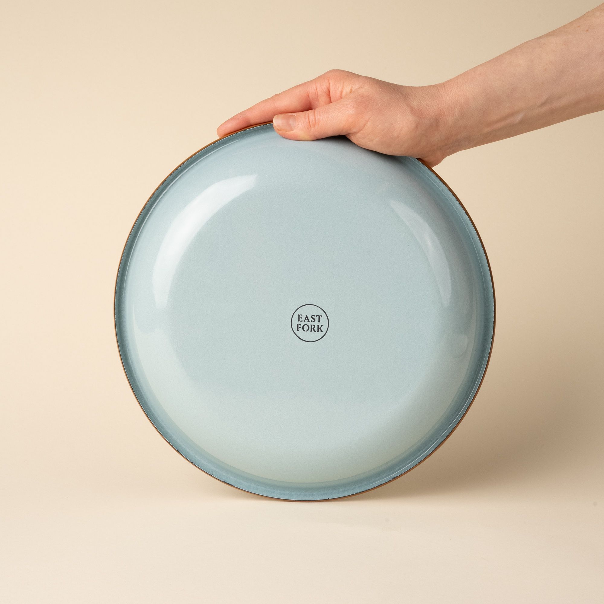 A hand holds up the back of a robin's egg blue enamel plate with a stamp that reads 'East Fork'