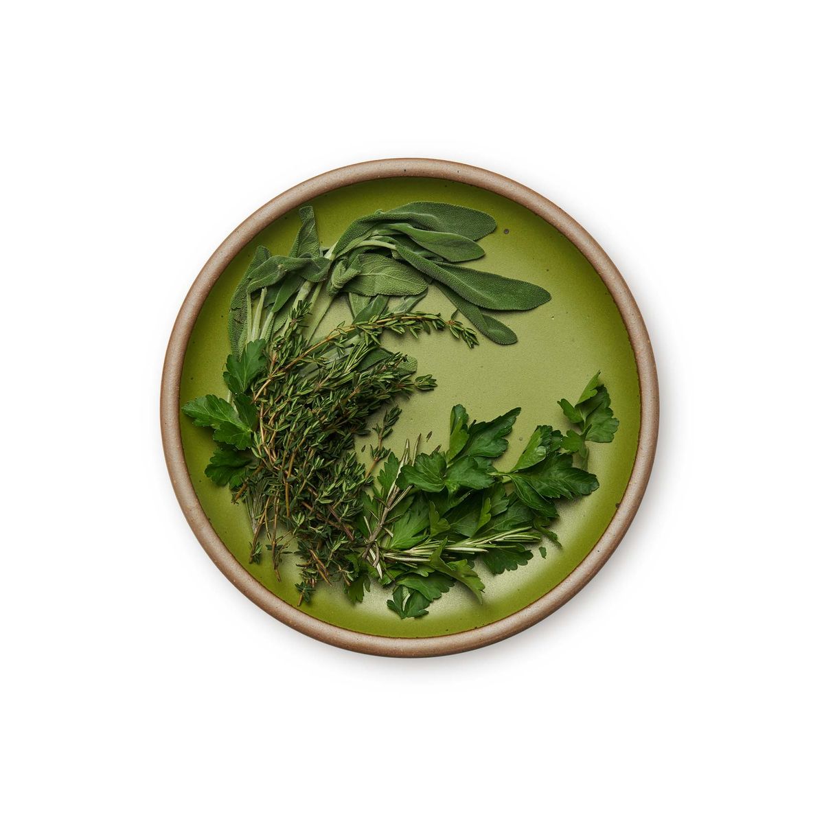 Dinner Plate in Fiddlehead, a mossy, olive green. Pictured with a plate of herbs.