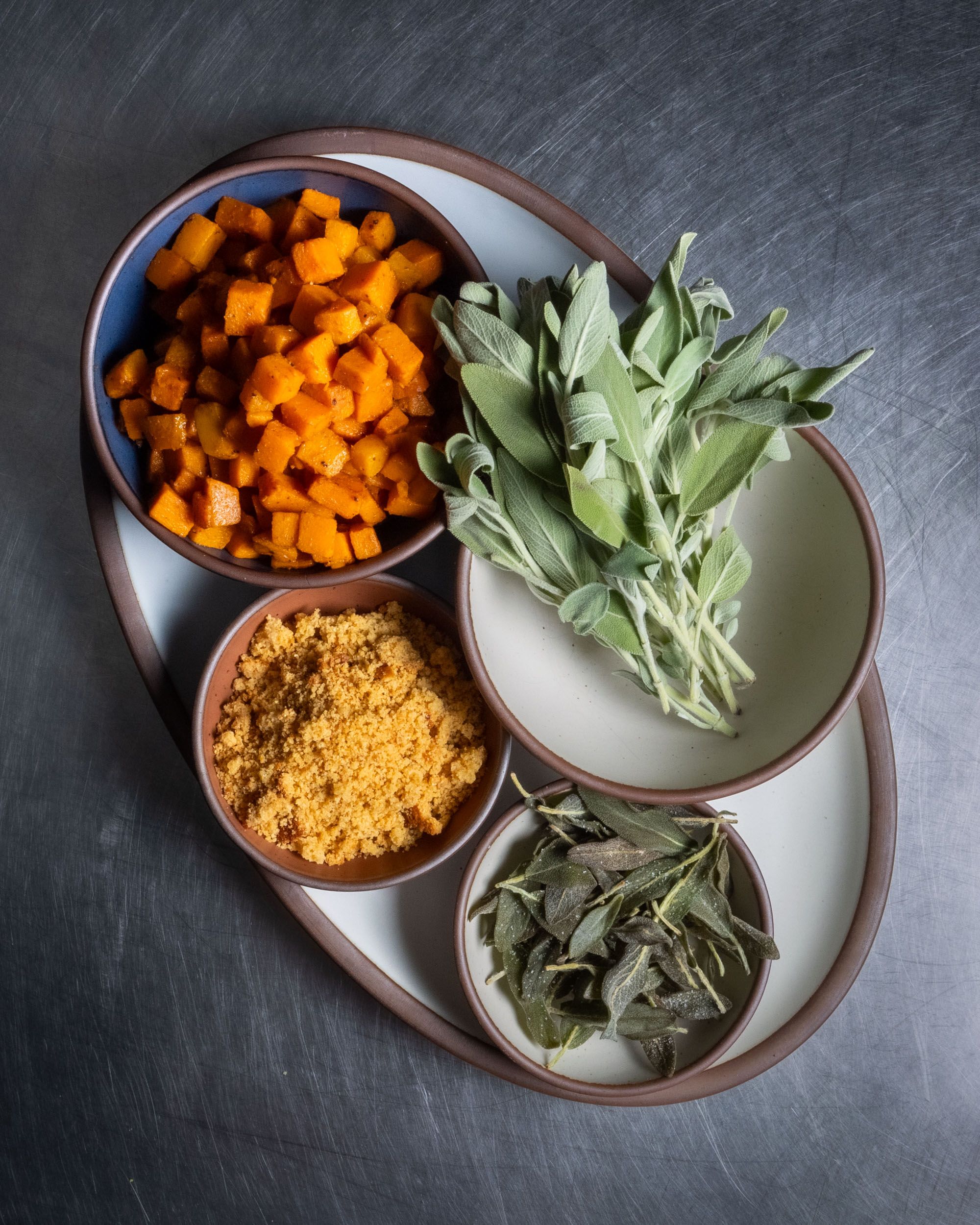 White ceramic plates and bowls hold different ingredients including chopped butternut squash and herbs and spices