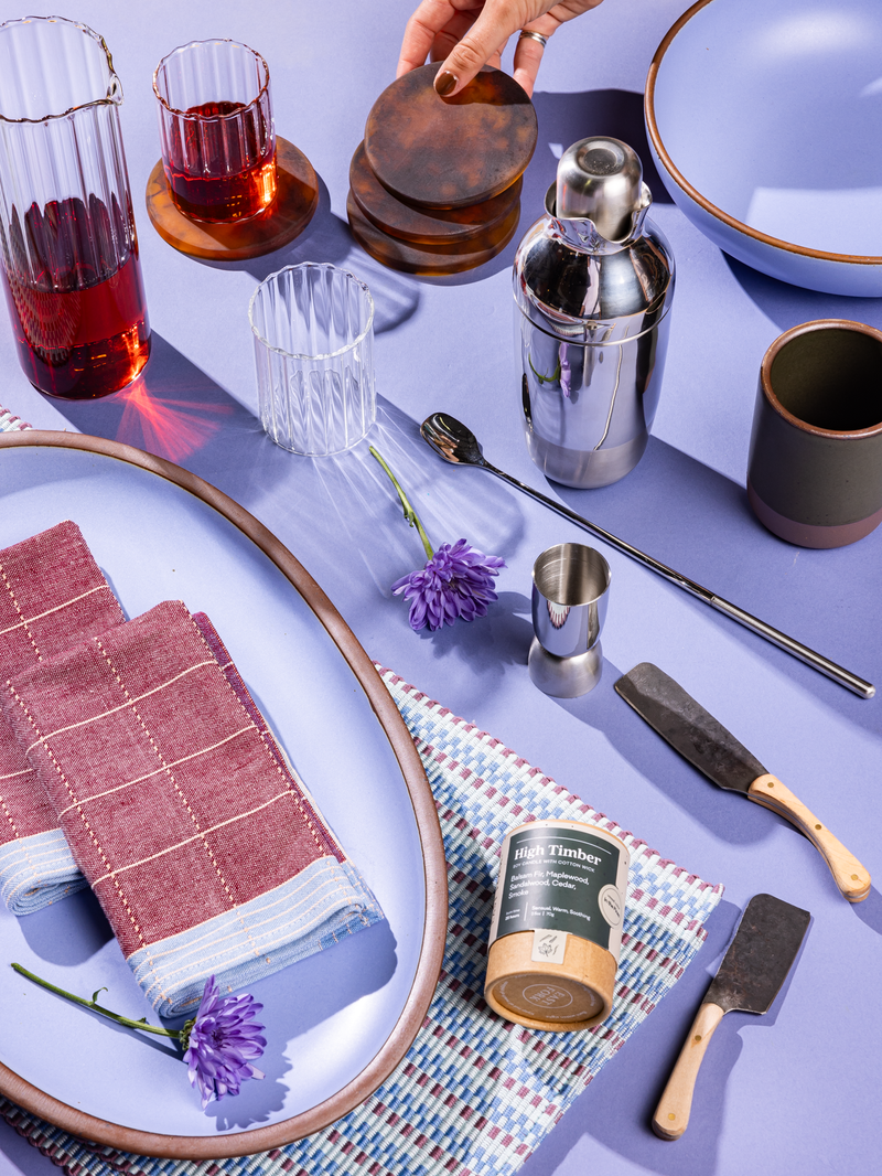 A collection of gifts including a cocktail shaker set, glassware, a mug, a large oval platter, and more against a periwinkle background.