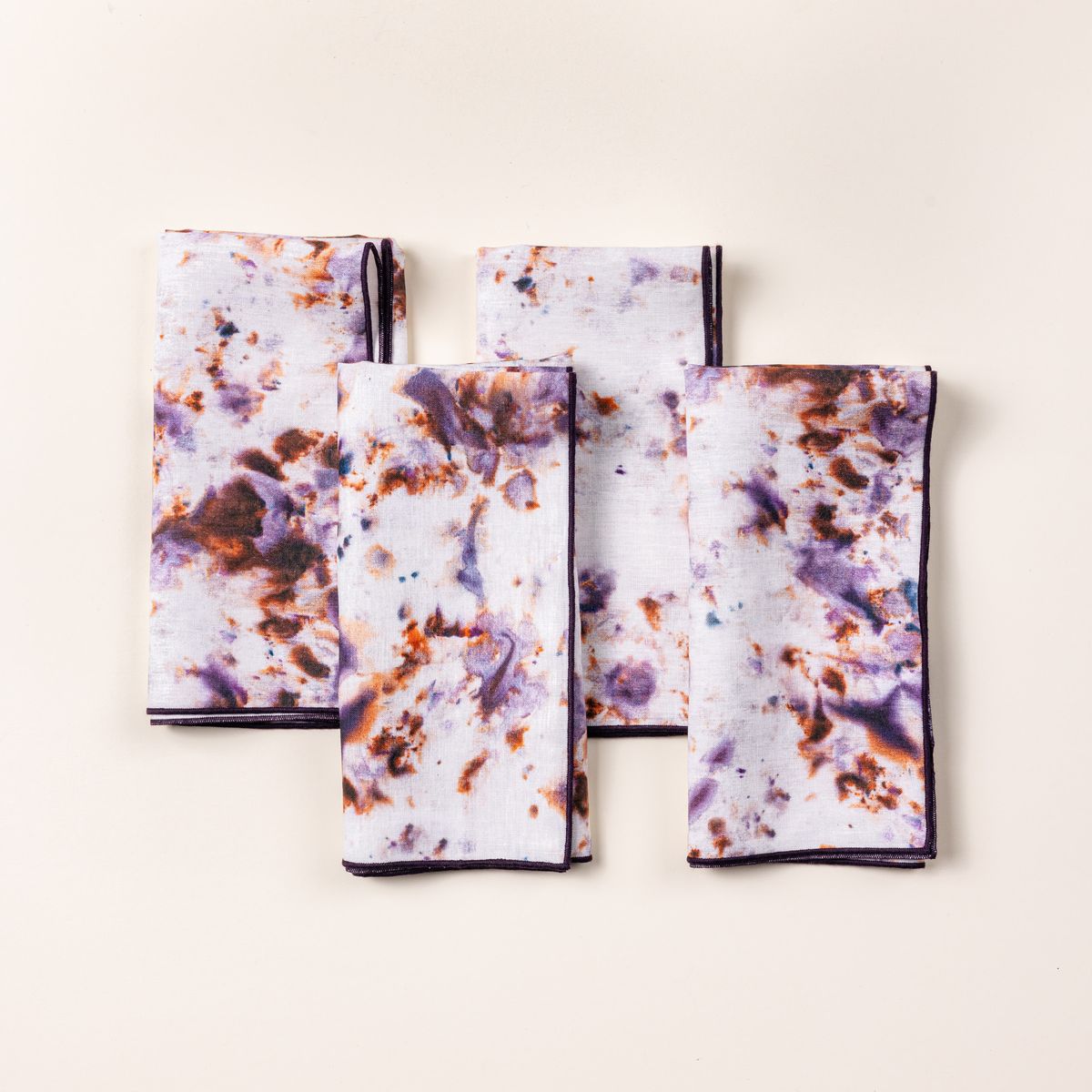 4 folded linen napkins in a marbled pattern with white, pink, purple, and orange colors