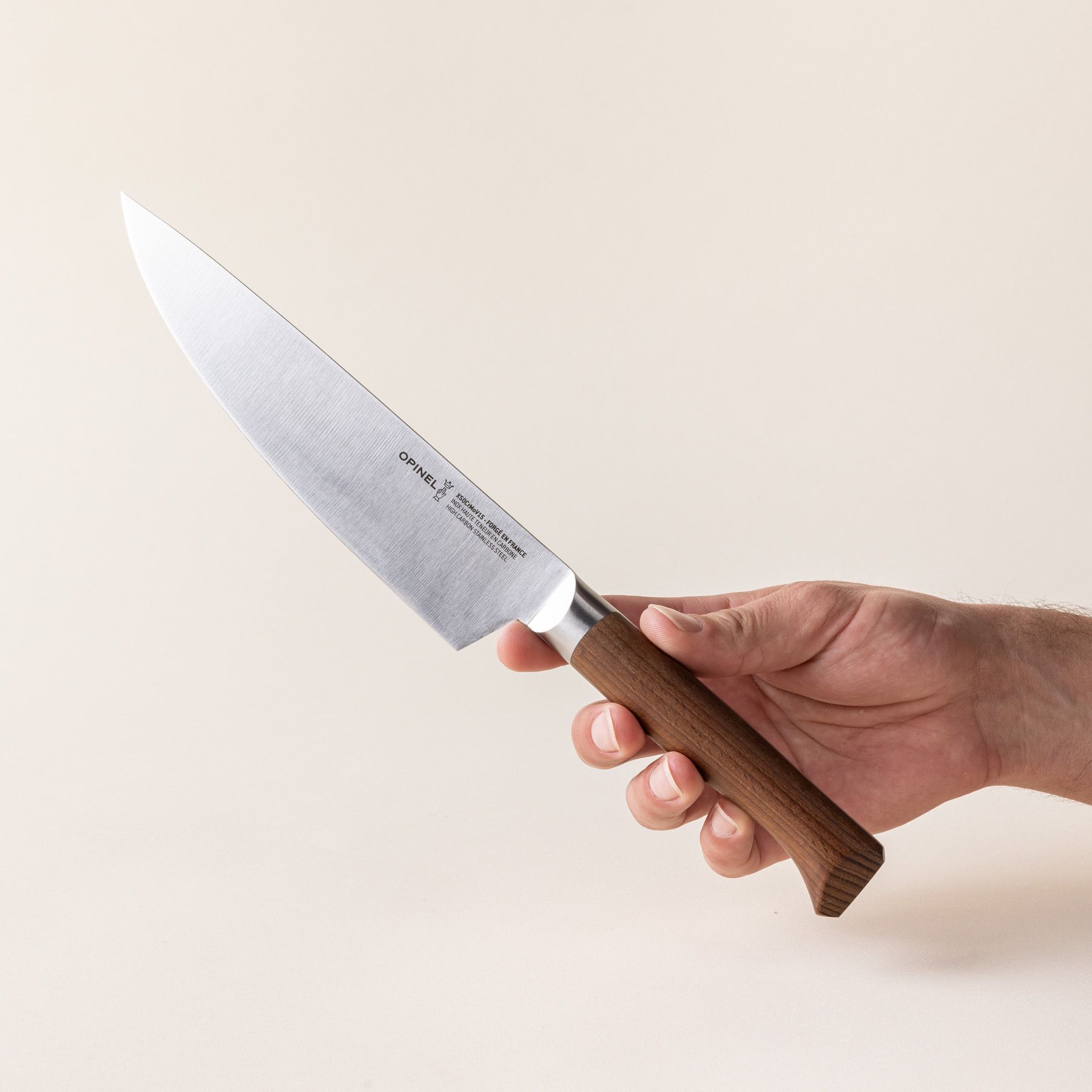 A hand holds a chef's knife with a sharp steel blade with a beveled dark wood handle