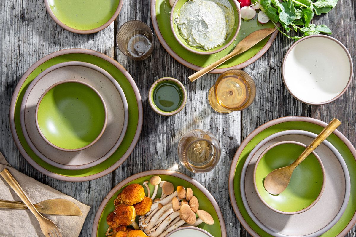 A spring-time table setting with green, brown and off-white pottery, brass flatware, and handblown glass. 