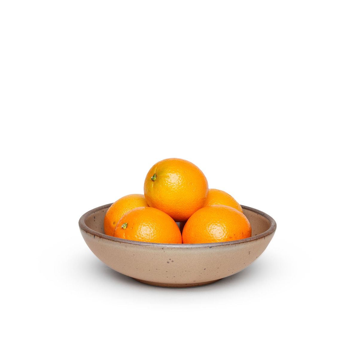 A dinner-sized shallow ceramic bowl in a warm pale brown color featuring iron speckles and an unglazed rim, filled with oranges