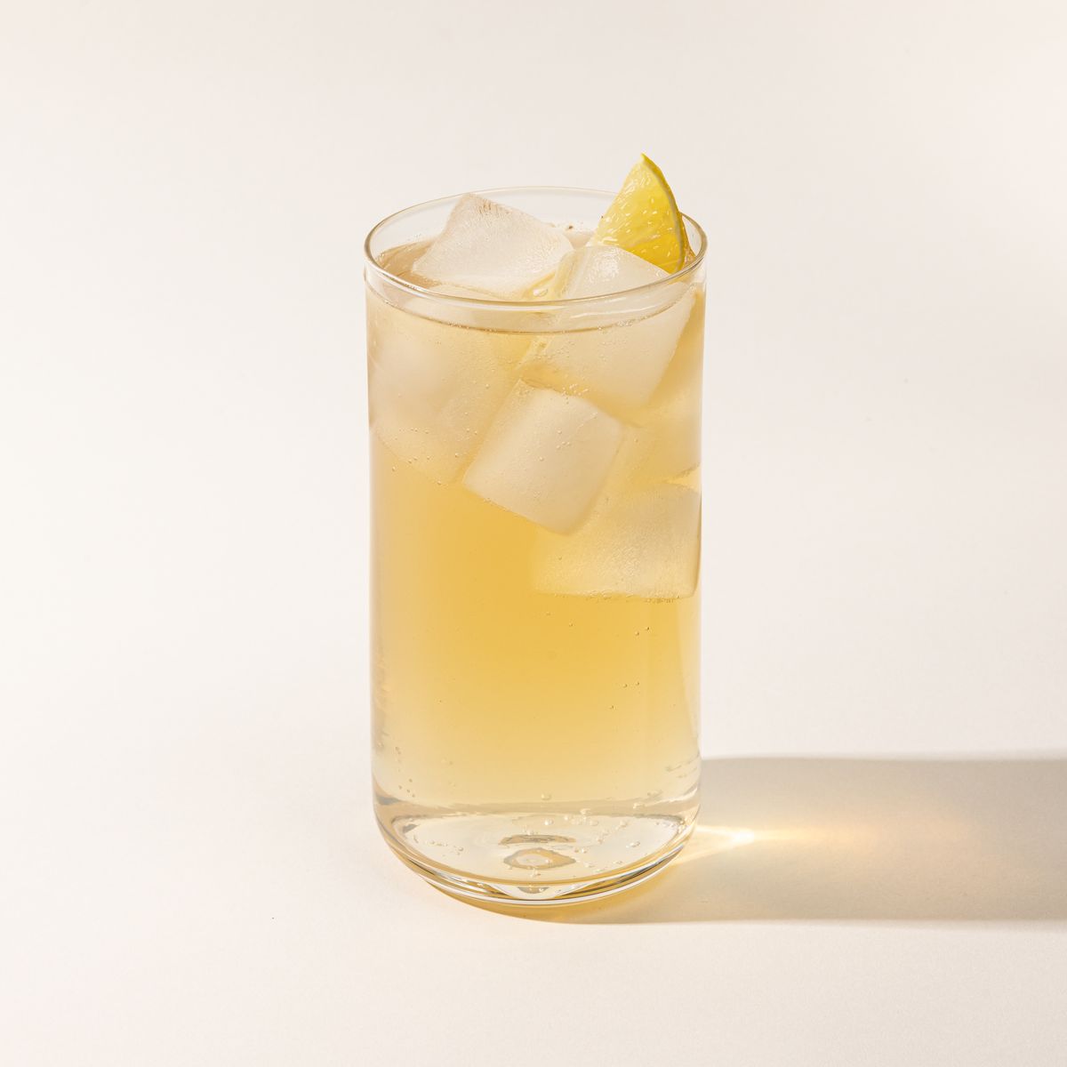A straight walled tall glass cup with a yellow cocktail and lemon garnish.