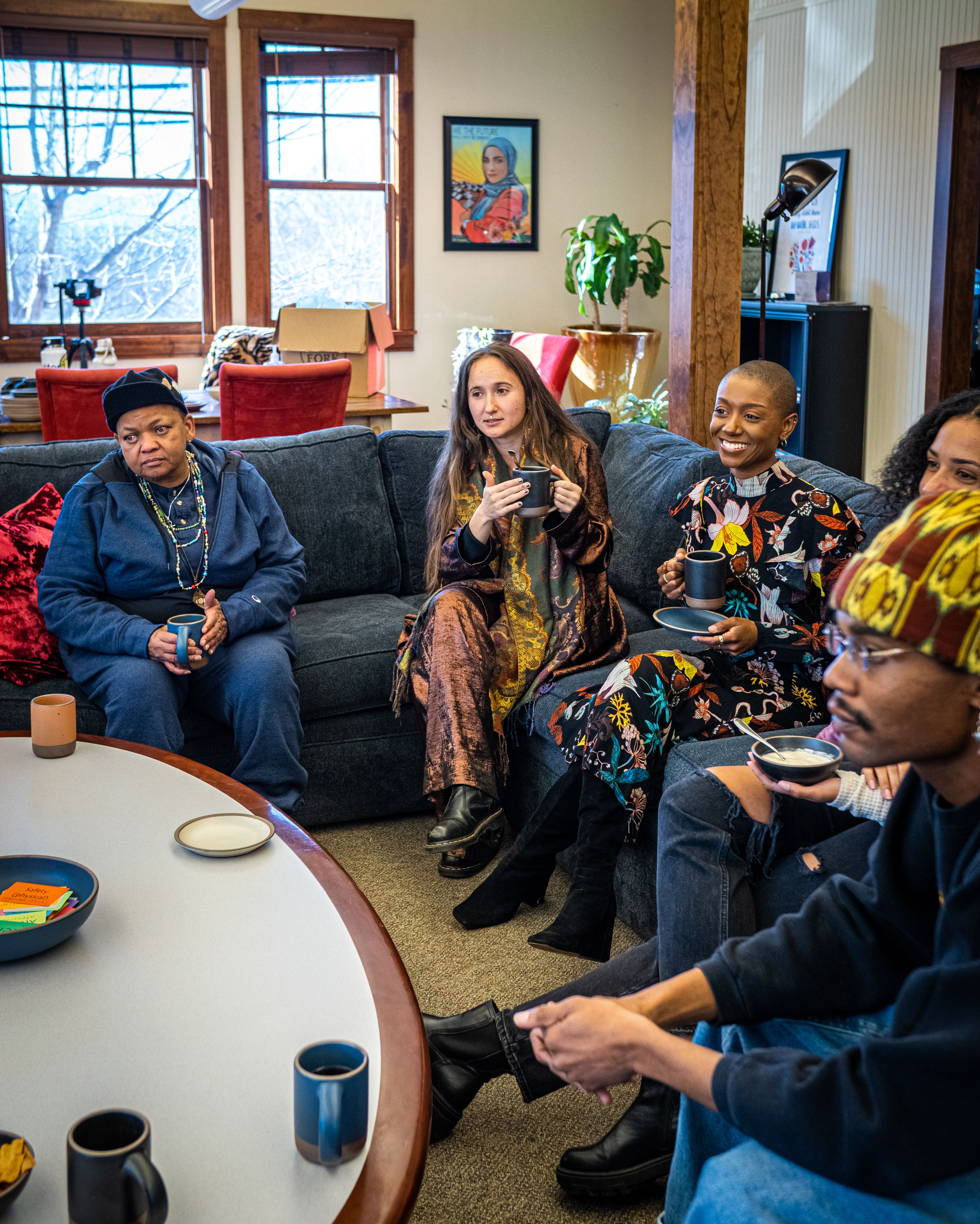 A diverse group of people are gathered inside on a sectional couch in conversation around a table