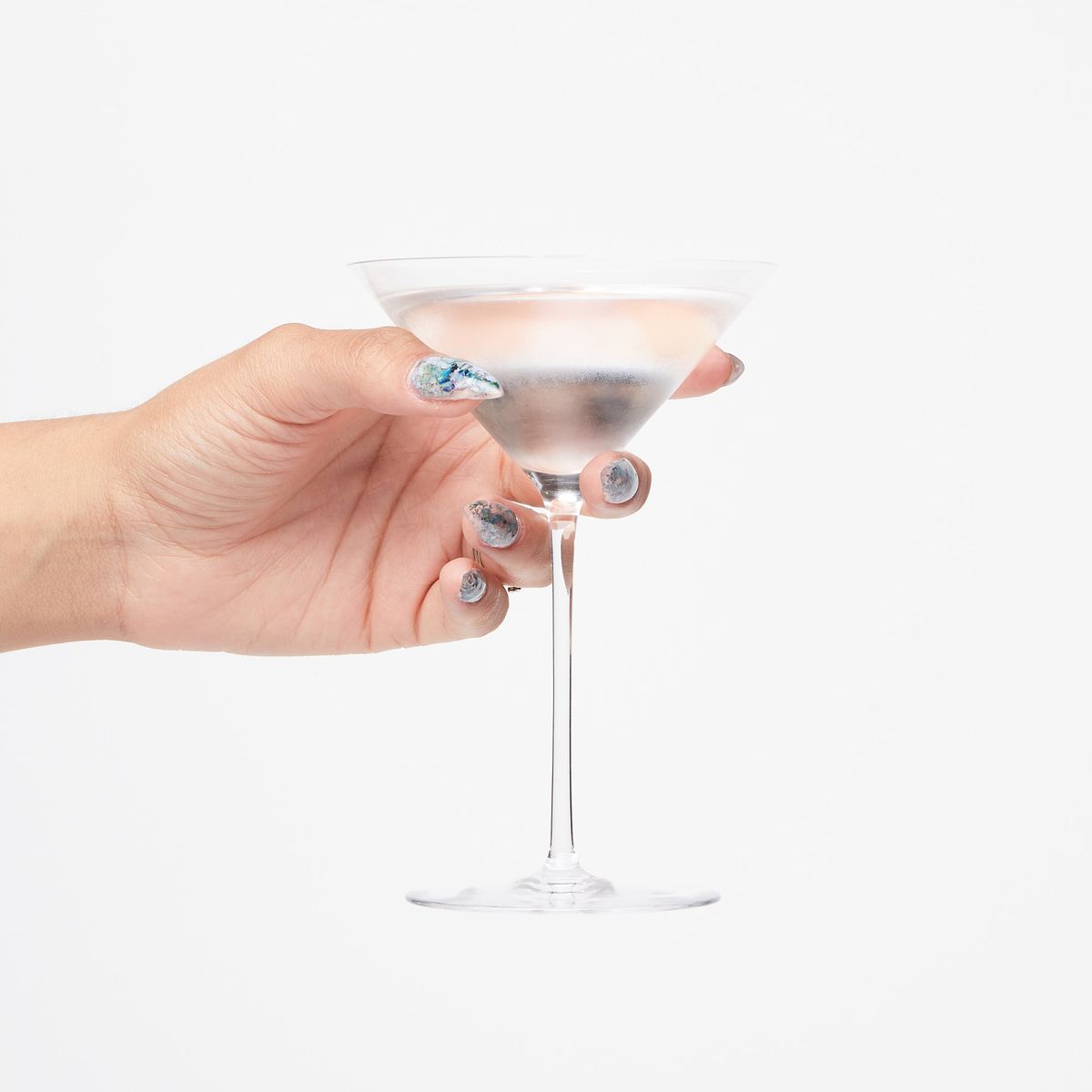 Hand holding a martini glass full of a clear liquid with condensation on the outside