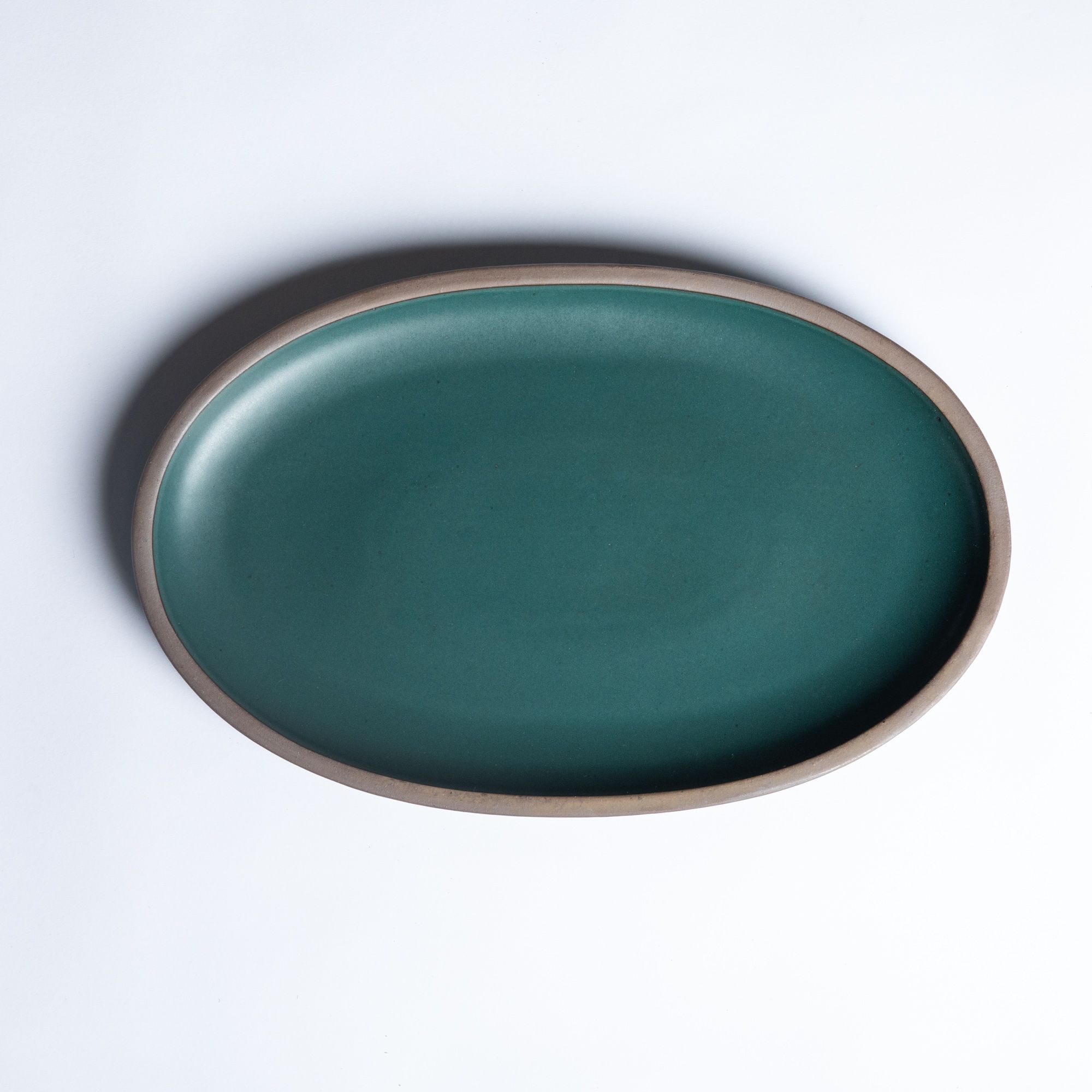 A large oval ceramic platter in a deep, dark teal color featuring iron speckles and an unglazed rim