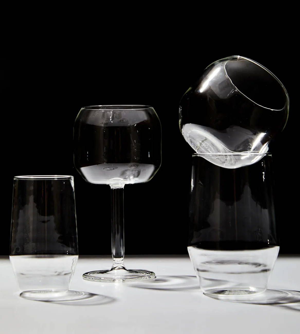 4 clear drinking glasses of various sophisticated shapes sit on a white surface with a black background.
