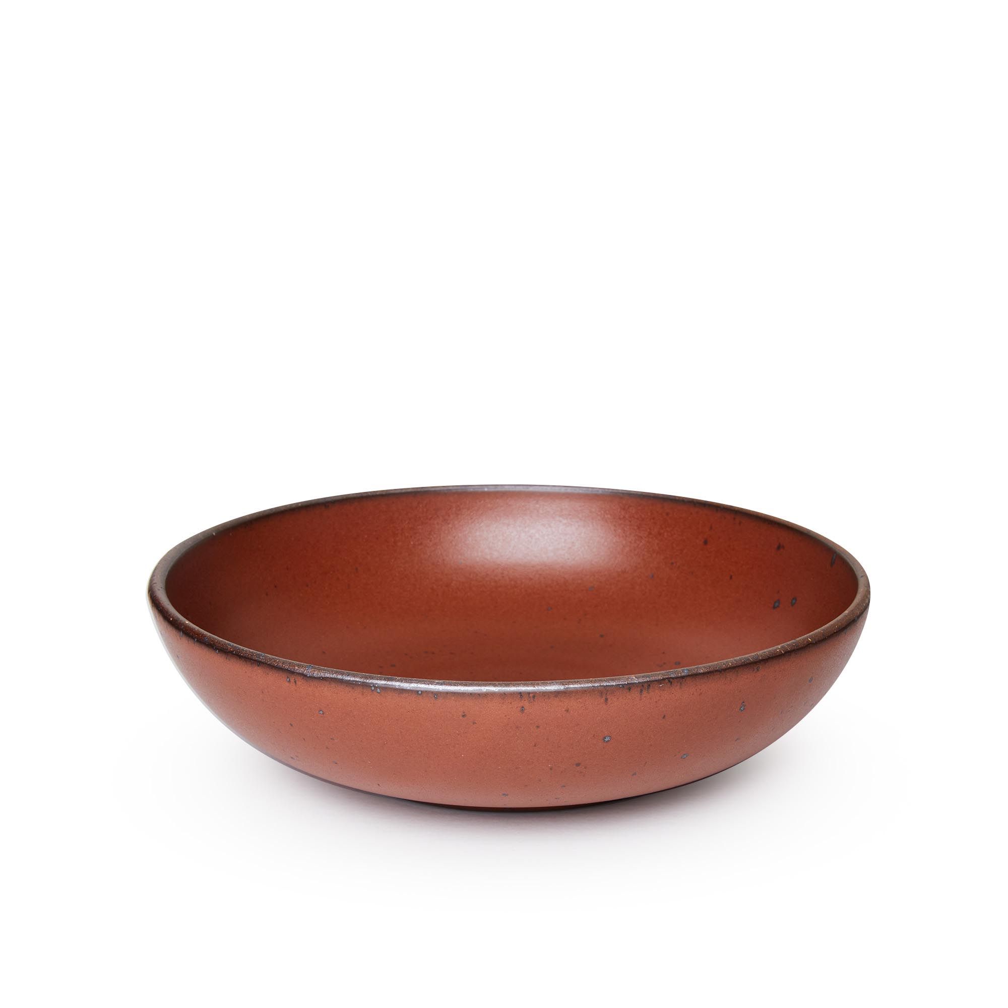 A large shallow serving ceramic bowl in a cool burnt terracotta color featuring iron speckles and an unglazed rim.