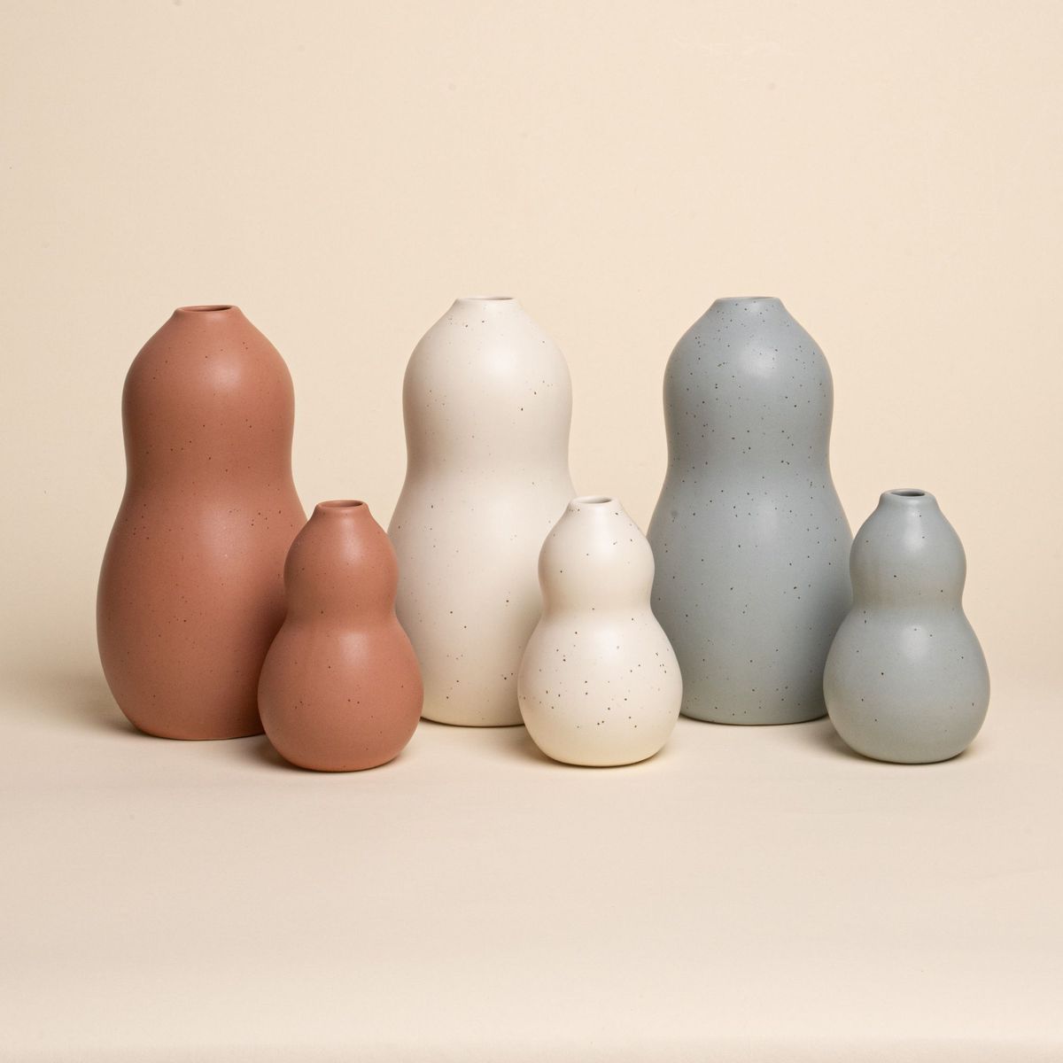 Set of six curvy ceramic vases in terracotta, cream, and blue-grey tones, arranged by size on a neutral background.