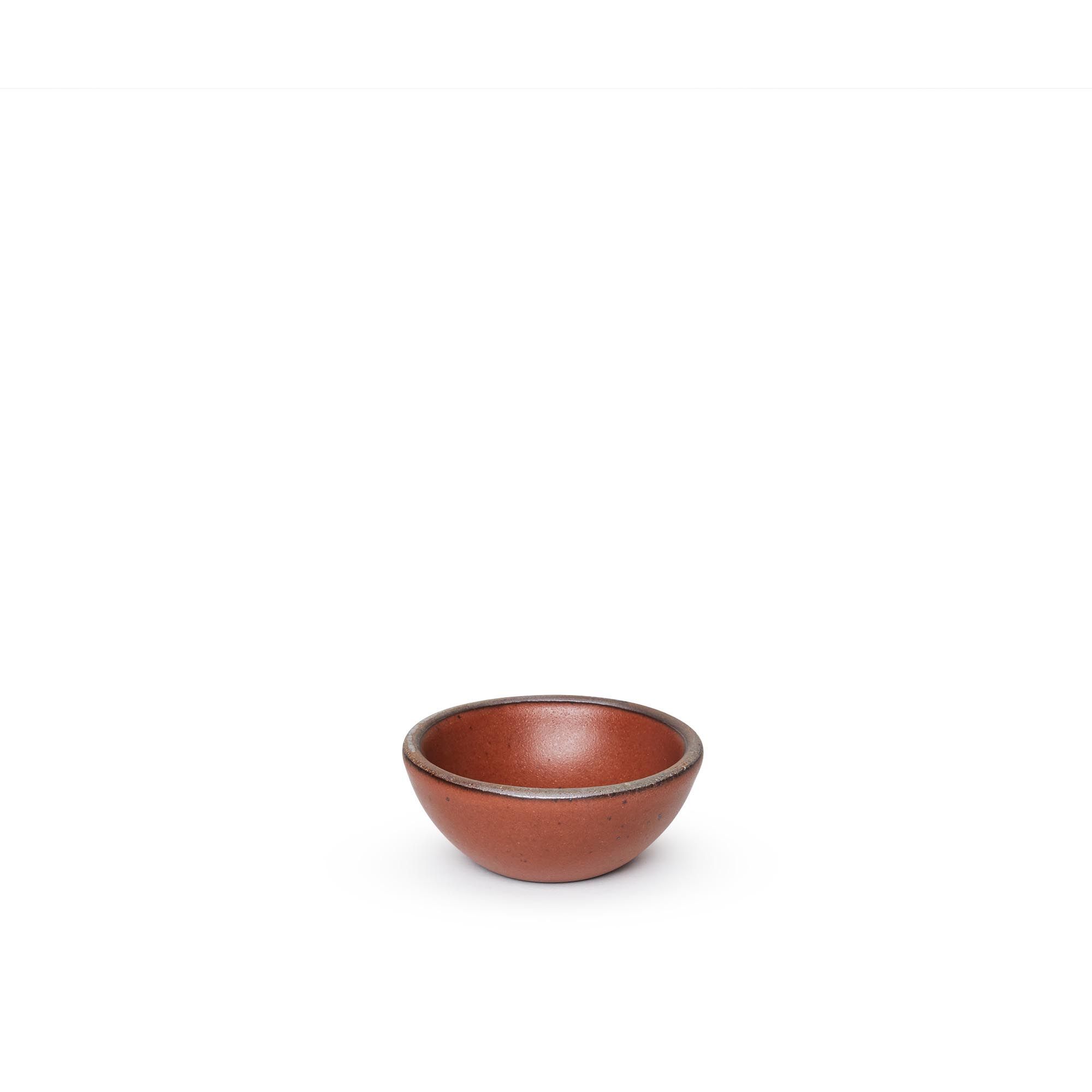 A tiny rounded ceramic bowl in a cool burnt terracotta color featuring iron speckles and an unglazed rim