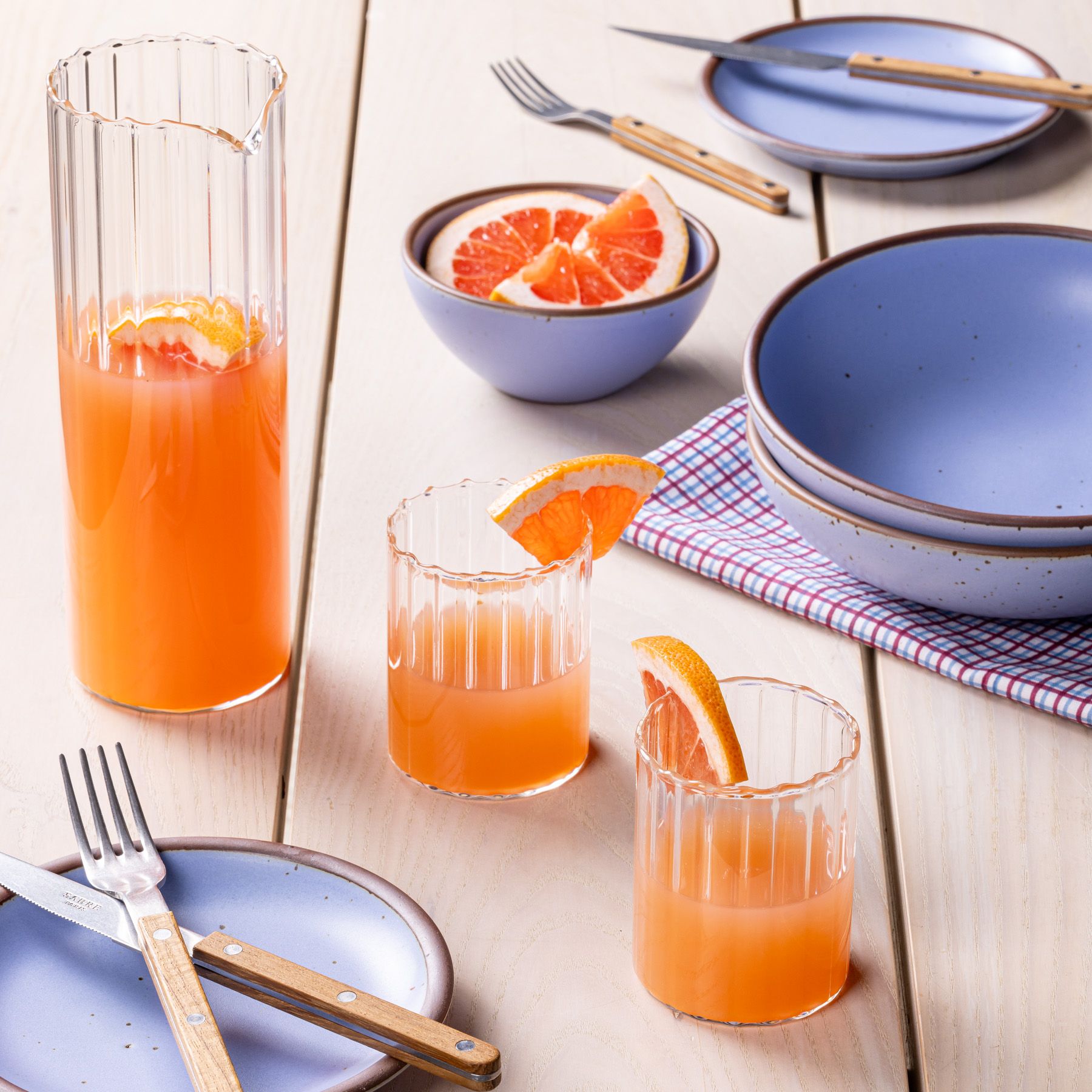 Fluted pitcher and short tumblers sit with periwinkle ceramic pots and plates with sliced grapefruits