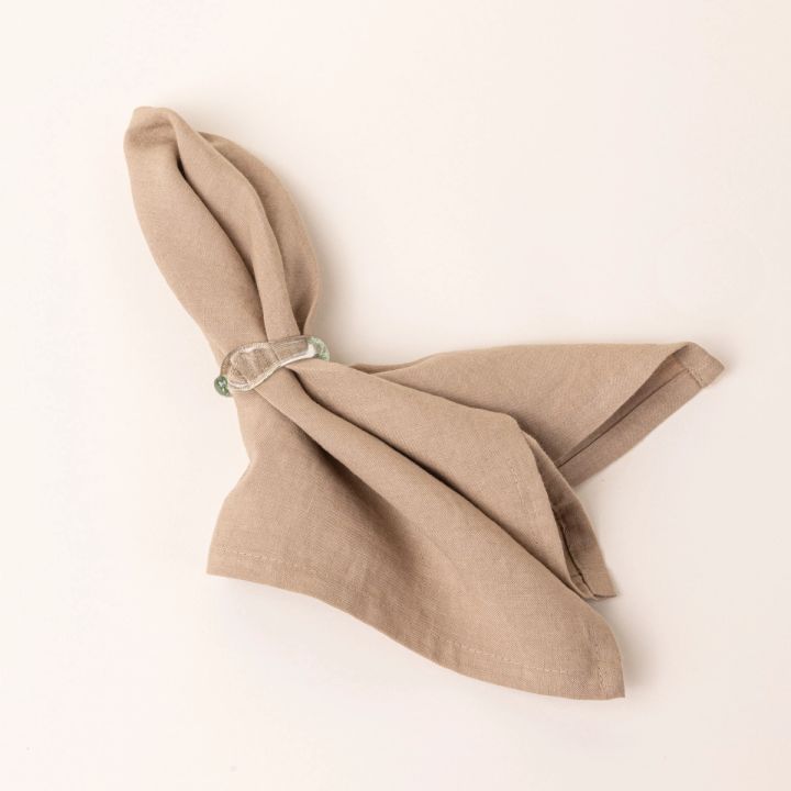 A glass napkin ring wrapped around a natural beige linen napkin