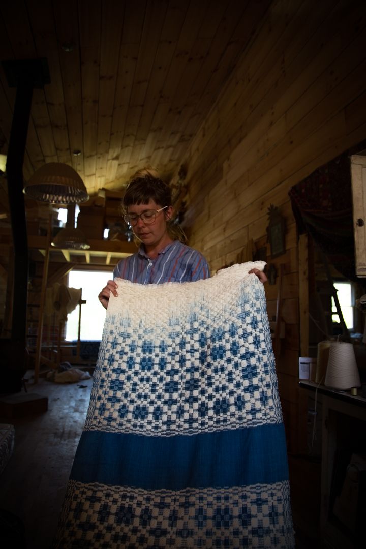 A woman holds up a large weaving in white and blue colors