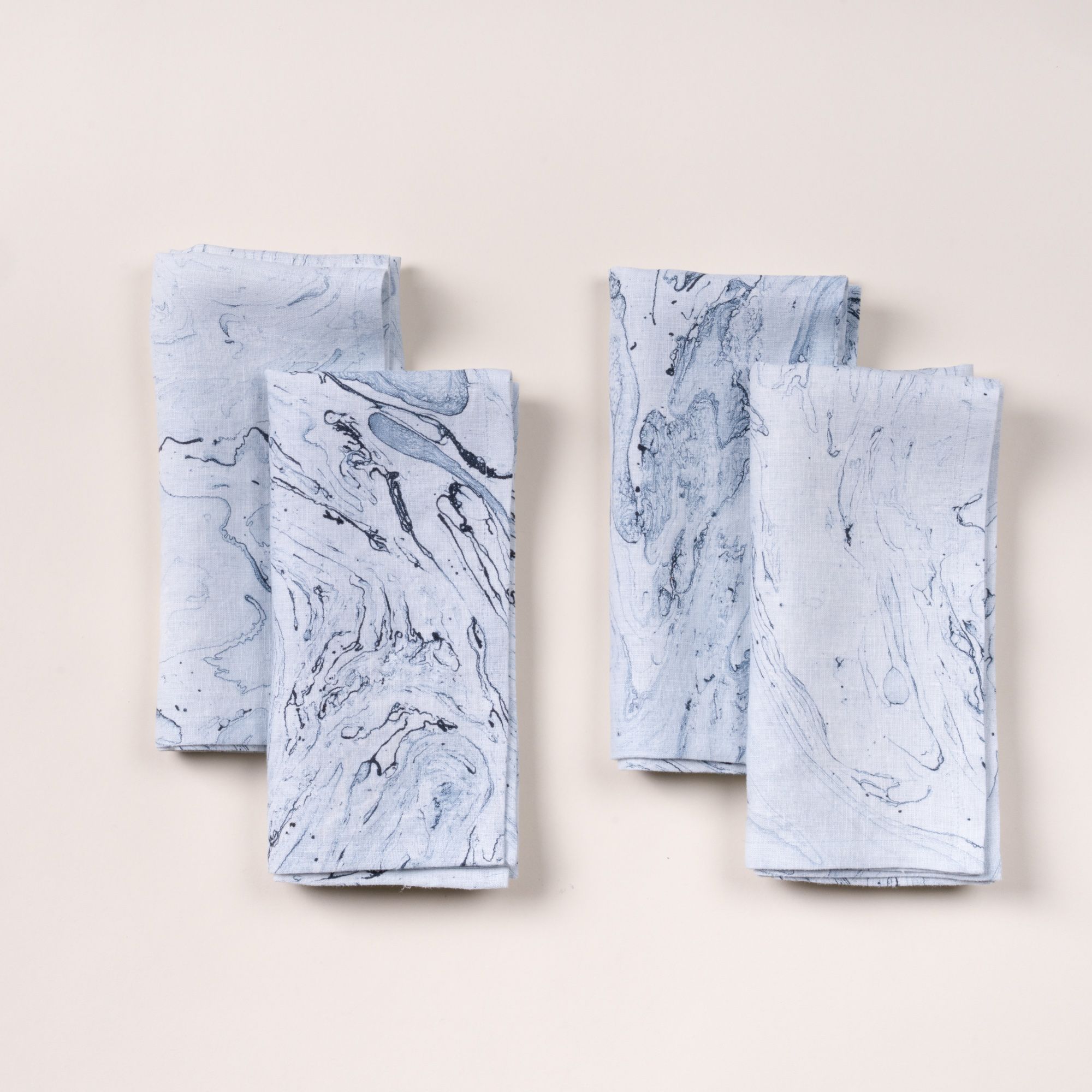 Four folded napkins with a blue marble-like pattern arranged on a light background.