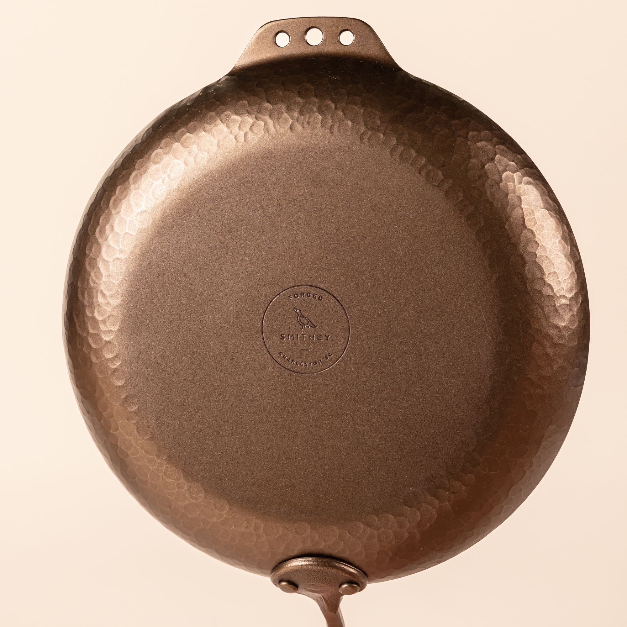 The bottom of a carbon steel farmhouse skillet with a hammered texture and hand forged design. The bottom features a stamp for the brand, Smithey.