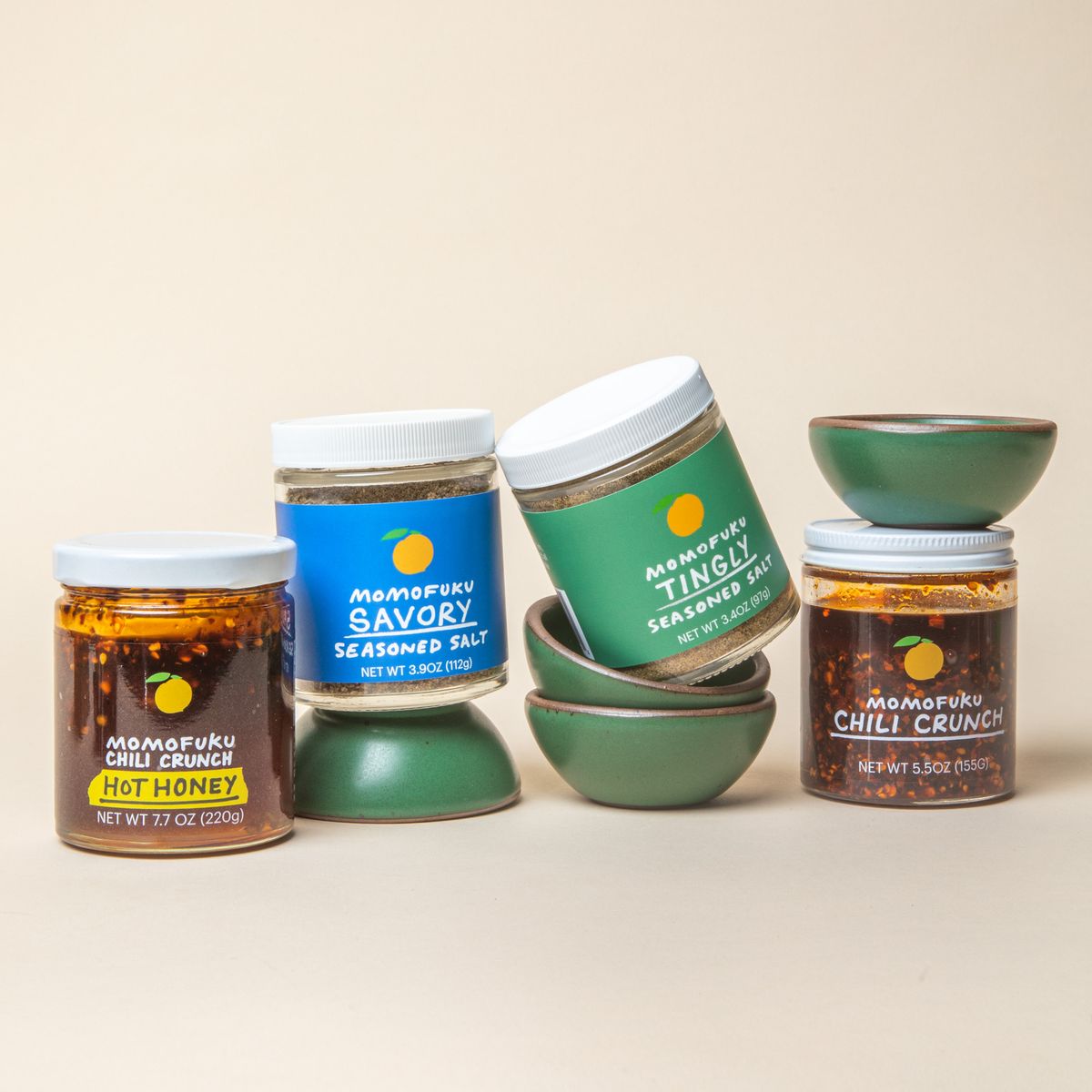 4 little ceramic bowls in a cool green color surrounded by 4 jars of Momofuku seasoned salts and chili crunch.