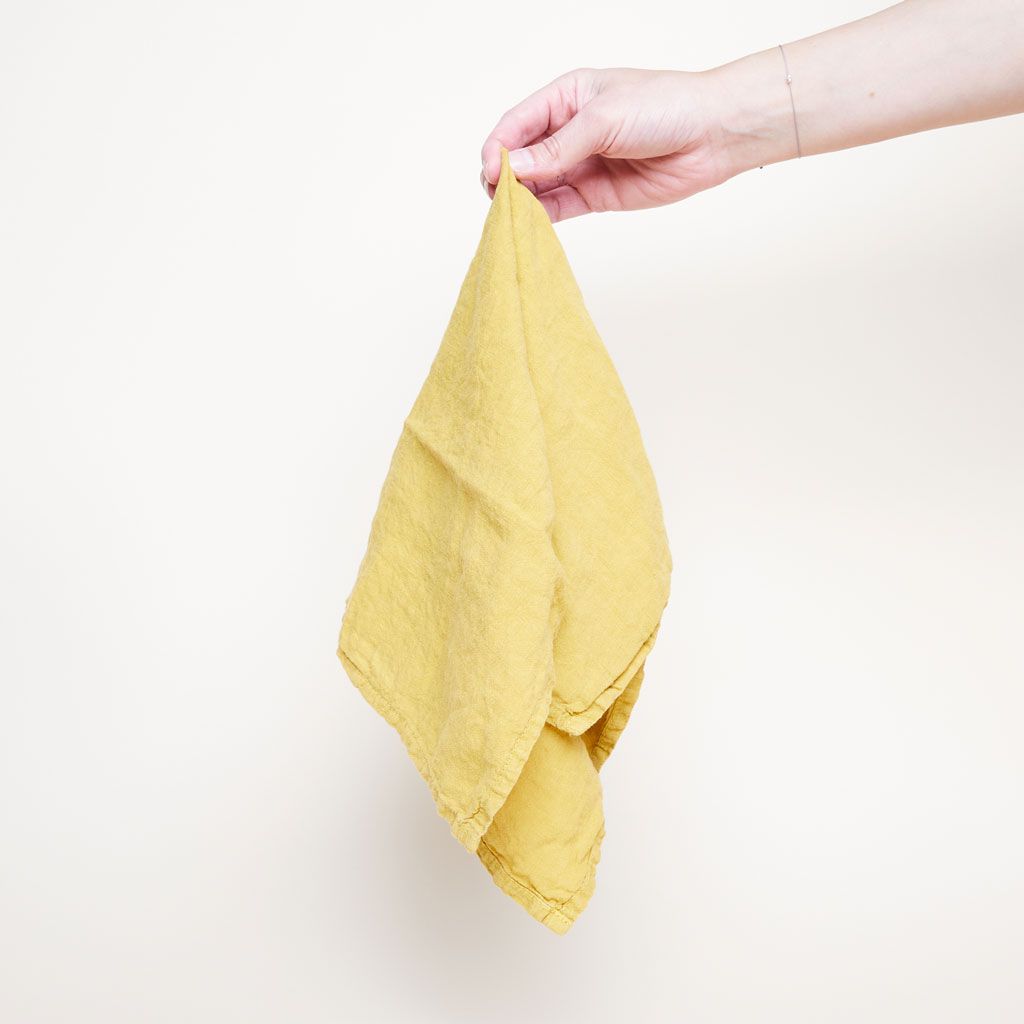 Fingers pinch the top of a linen napkin that is mustard colored