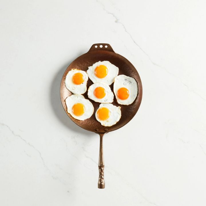 Six fried eggs on a carbon steel farmhouse skillet with a hammered texture and hand forged design