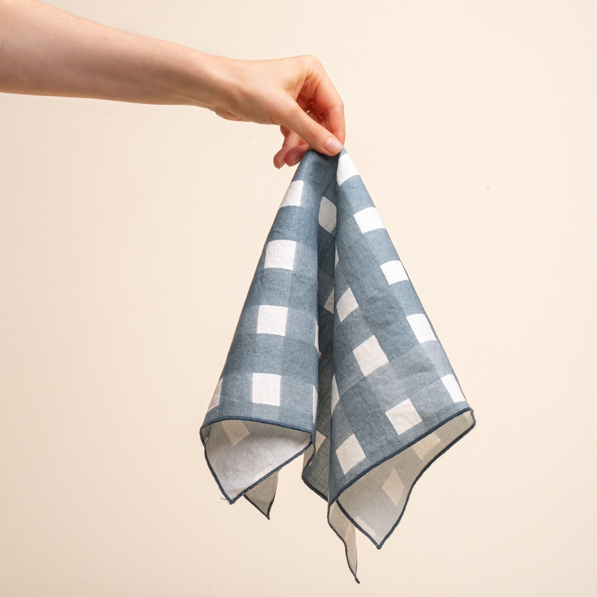 A hand holds up the center of a blue-grey crosshatch napkin